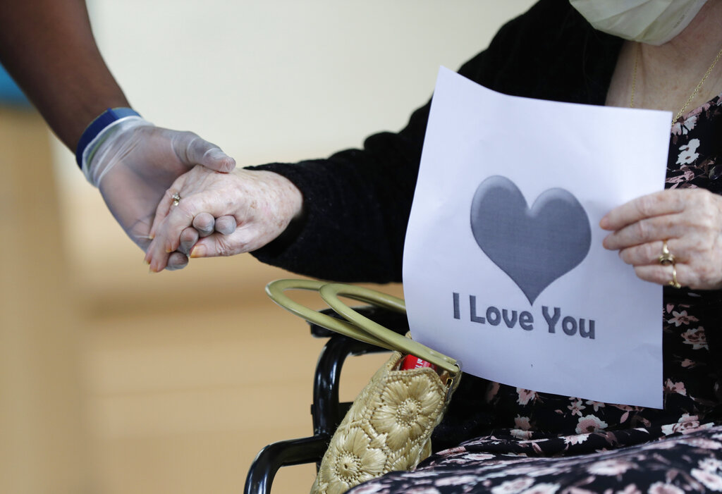 In this July 17, 2020 file photo, a senior citizen holds the hand of a care coordinator at a Health facility in Miami. (AP Photo/Wilfredo Lee)