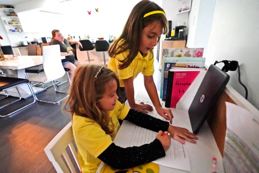 Emily Chao, standing, watches as her sister Anabelle, works on a writing exercise after they finished remote learning for the day on Oct. 1, 2020, at their home in North Miami Beach, Fla. Rather than wait to see how the Miami-Dade school system would handle instruction this fall, Erica Chao enrolled her two daughters in a private school that seemed better positioned to provide remote learning than their public elementary school was when the coronavirus first reached Florida. (AP Photo/Wilfredo Lee)