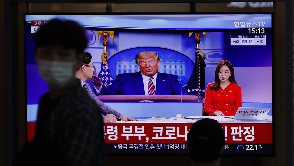 A man wearing a face mask walks near a TV screen reporting about U.S. President Donald Trump and first lady Melania Trump during a news program with a file image of Trump at the Seoul Railway Station in Seoul, South Korea, Friday, Oct. 2, 2020. (AP Photo/Lee Jin-man)