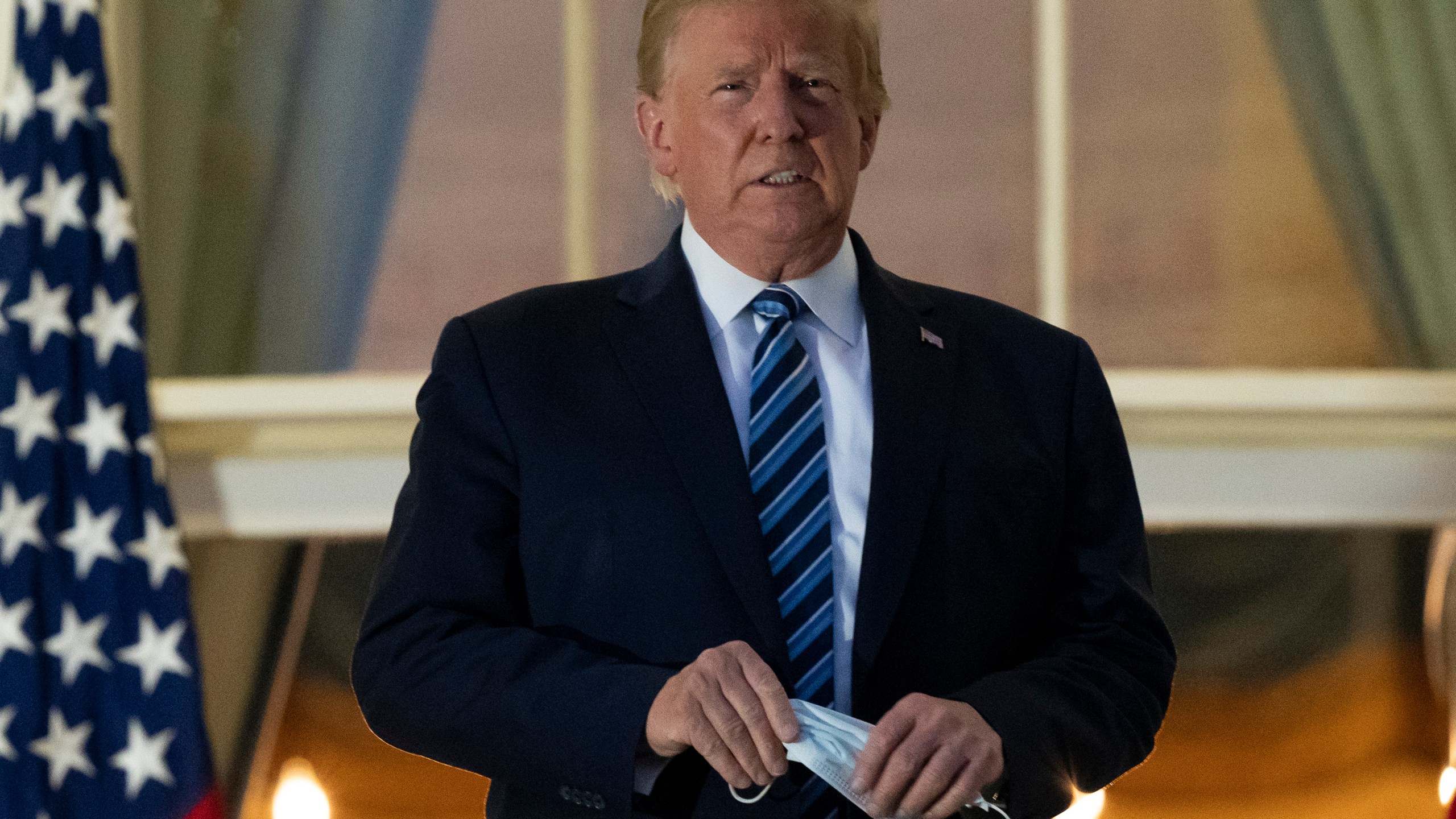 President Donald Trump holds his mask after removing it from his face as he stands on the Blue Room Balcony upon returning to the White House from the Walter Reed military hospital on Oct. 5, 2020. (Alex Brandon / Associated Press)