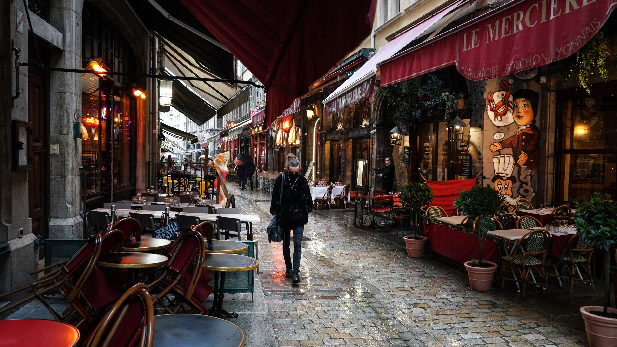 In this Friday, Oct. 2, 2020 file photo, a woman walks by empty restaurants in the center of Lyon, central France. (AP Photo/Laurent Cipriani, File)