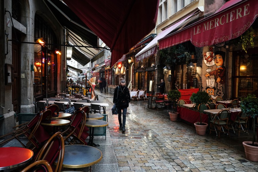 In this Friday, Oct. 2, 2020 file photo, a woman walks by empty restaurants in the center of Lyon, central France. (AP Photo/Laurent Cipriani, File)