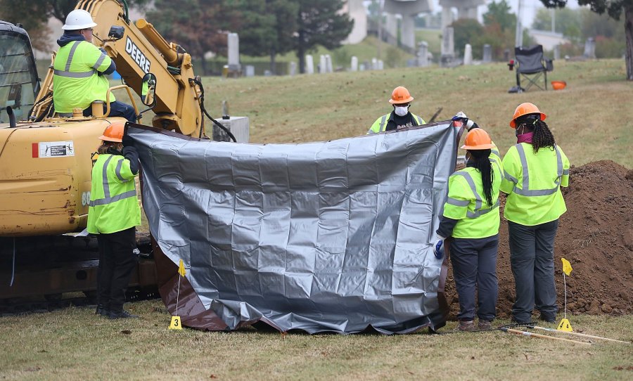 Workers hold up tarps to block spectators' views during a second test excavation and core sampling, Tuesday, Oct. 20, 2020, in the search for remains at Oaklawn Cemetery in Tulsa, Okla., from the 1921 Tulsa Race Massacre. (Mike Simons/Tulsa World via AP)