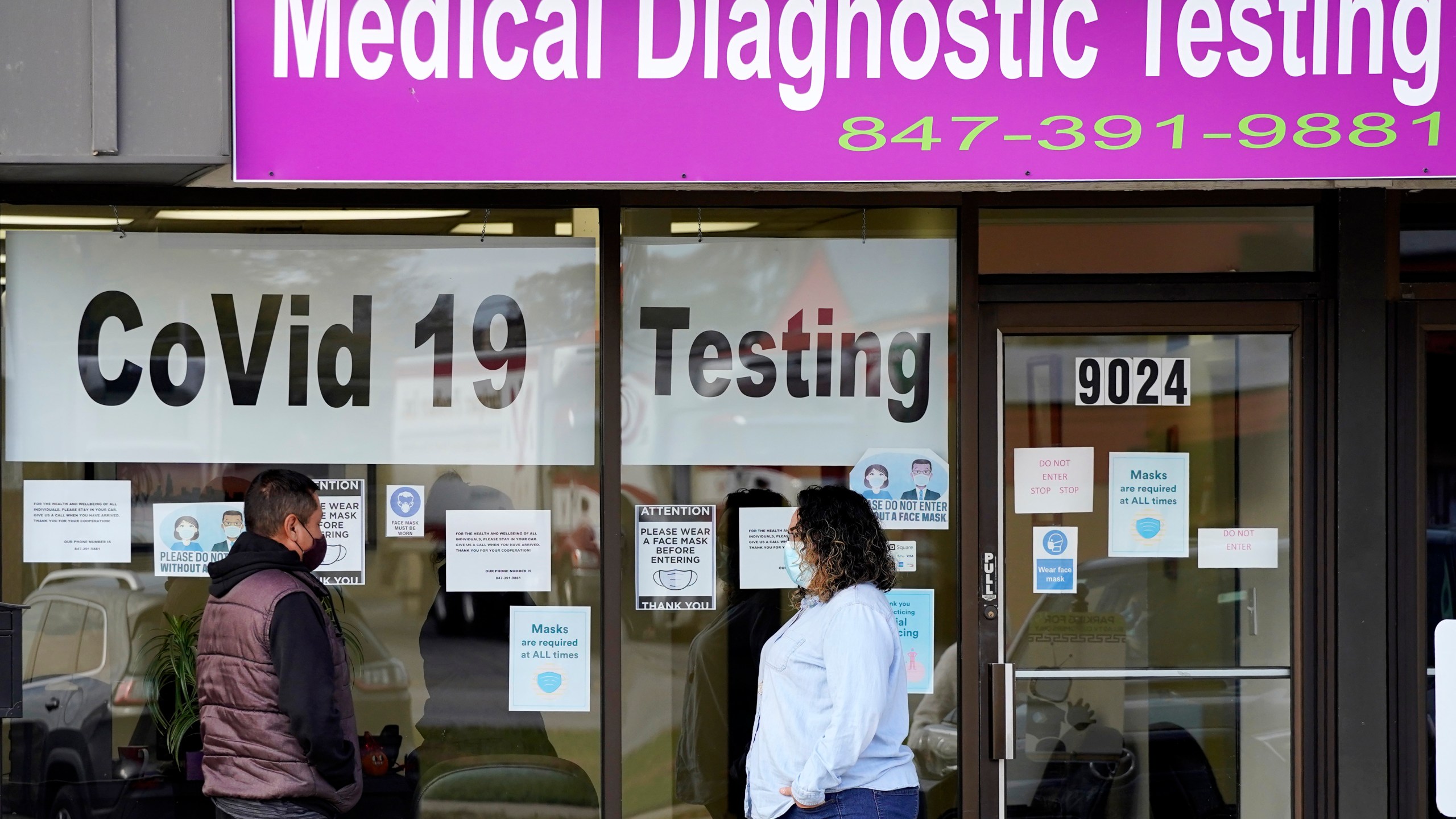 In this Oct. 21, 2020, file photo, Exam Corp Lab employee, right, wears a mask as she talks with a patient lined up for COVID-19 testing in Niles, Ill. The United States is approaching a record for the number of new daily coronavirus cases in the latest ominous sign about the disease's grip on the nation. (AP Photo/Nam Y. Huh, File)