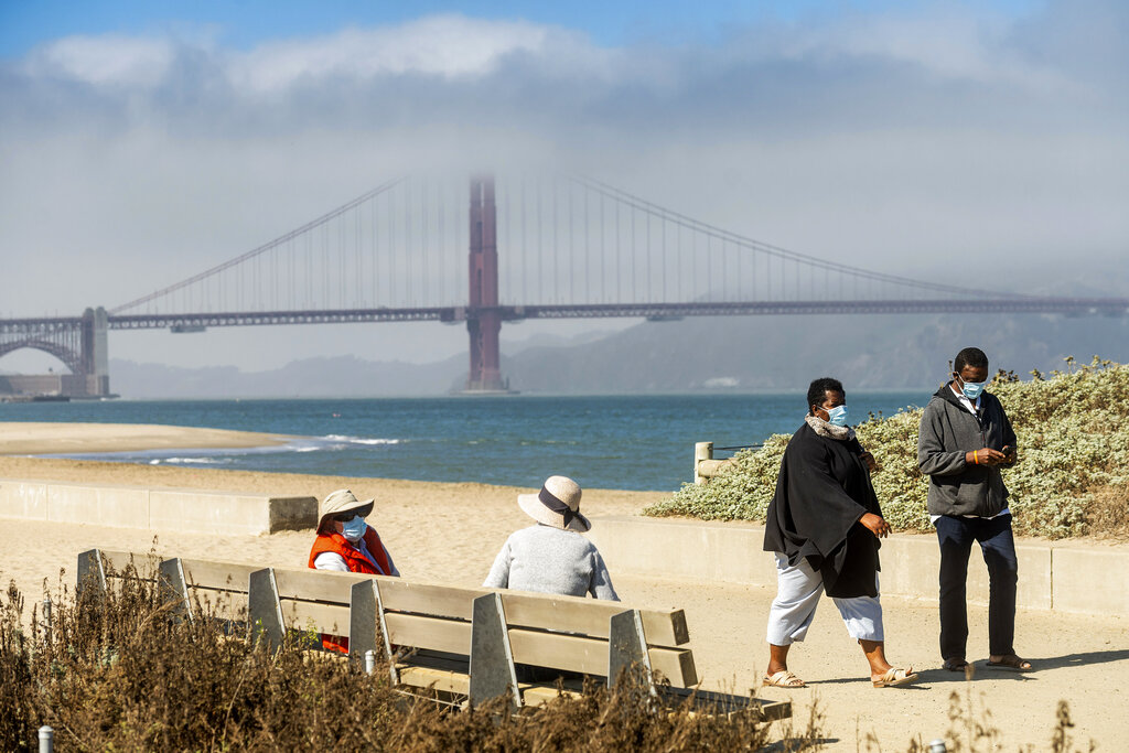 With the Golden Gate Bridge in the background, walkers wear masks while strolling at Crissy Field East Beach in San Francisco on Oct. 22, 2020. (AP Photo/Noah Berger)