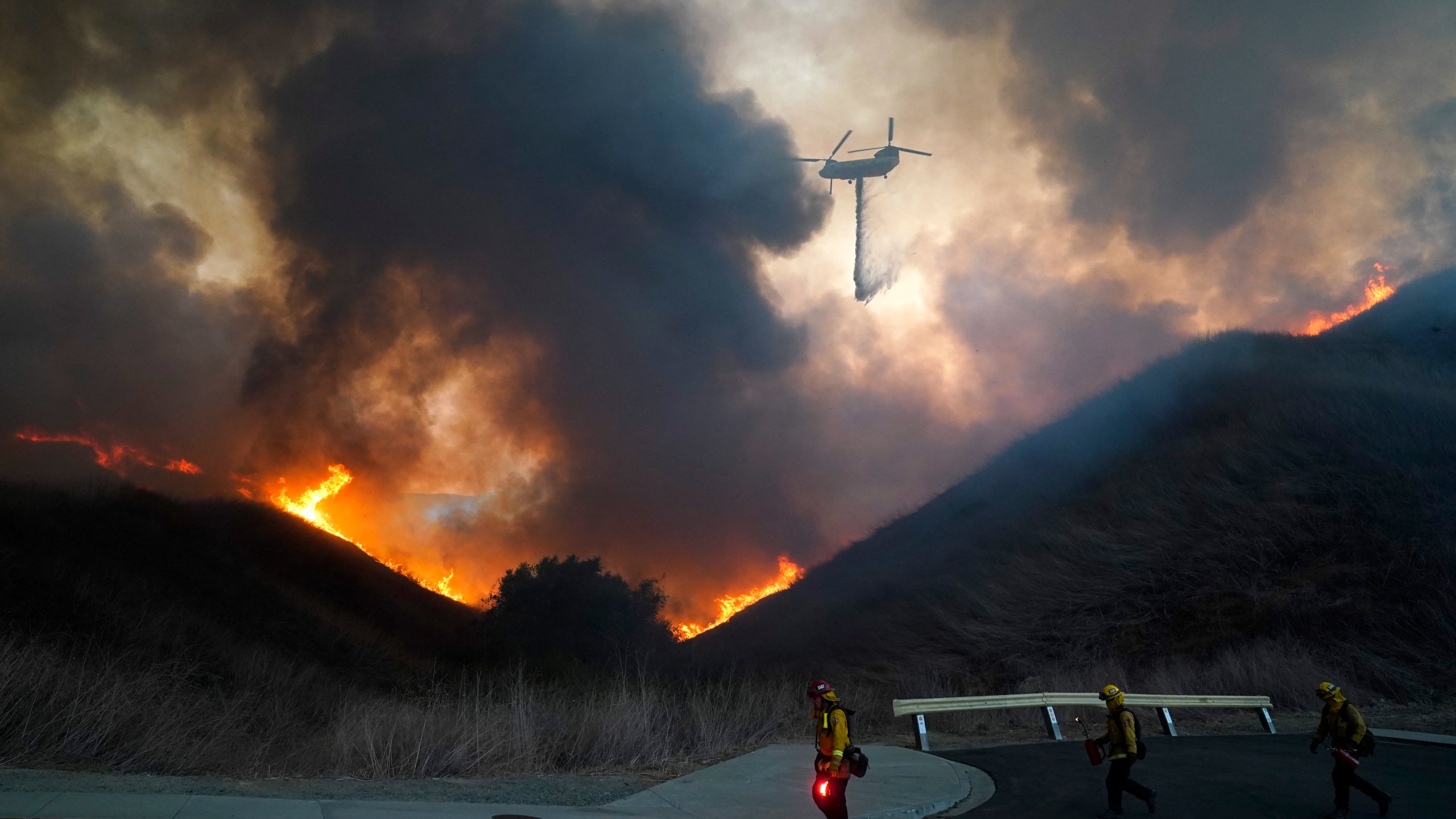 A helicopter drops water as firefighters walk with drip torches to set a backfire against the Blue Ridge Fire on Oct. 27, 2020, in Chino Hills. (Jae C. Hong / Associated Press)