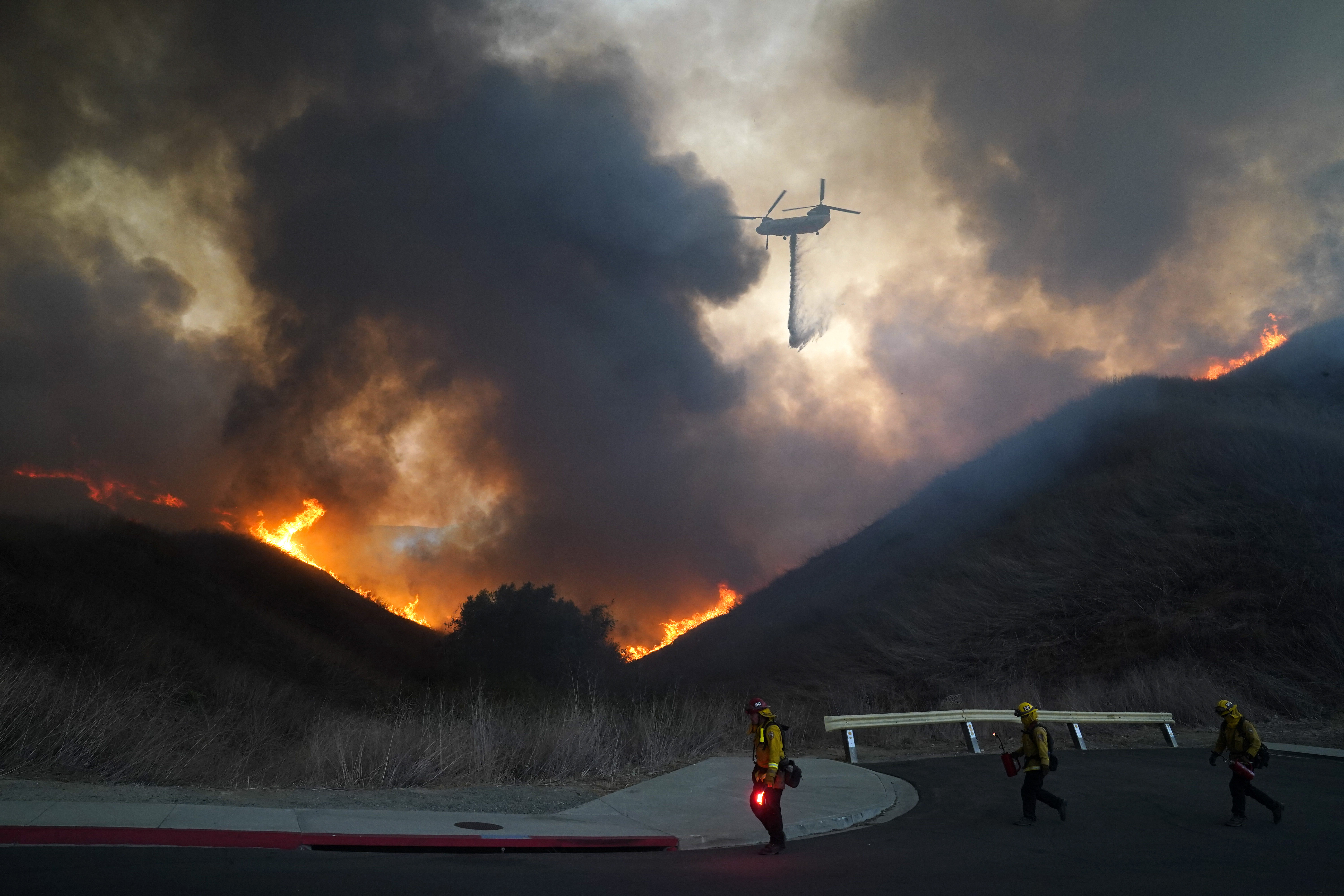 A helicopter drops water as firefighters walk with drip torches to set a backfire against the Blue Ridge Fire on Oct. 27, 2020, in Chino Hills. (Jae C. Hong / Associated Press)