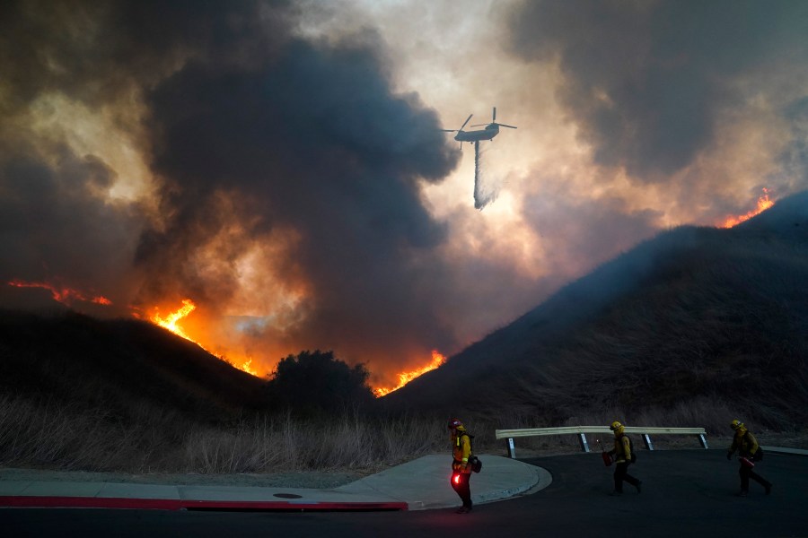 A helicopter drops water as firefighters walk with drip torches to set a backfire against the Blue Ridge Fire on Oct. 27, 2020, in Chino Hills. (Jae C. Hong / Associated Press)