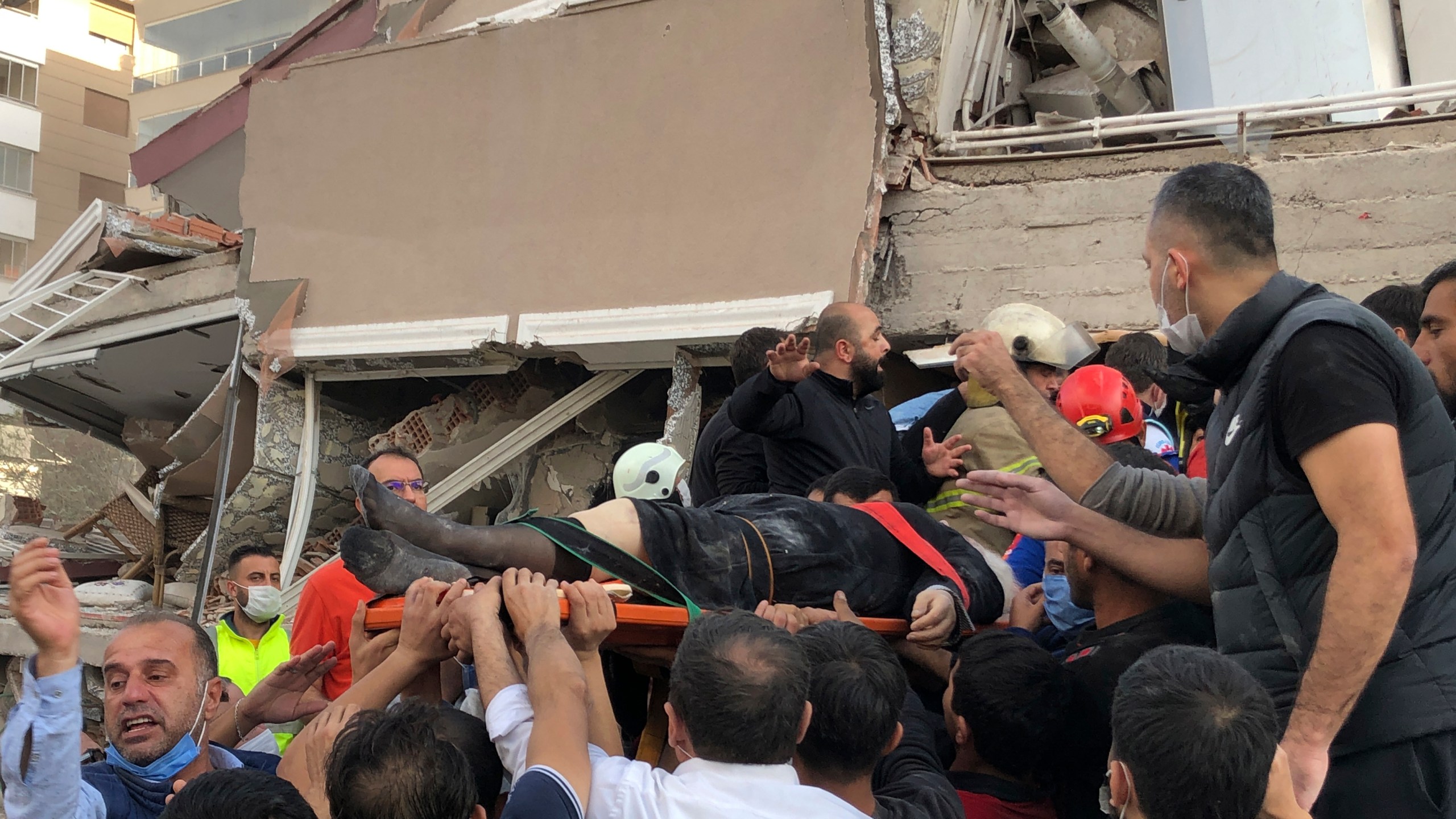 Rescue workers and local people carry a wounded person found in the debris of a collapsed building, in Izmir, Turkey, on Oct. 30, 2020, after a strong earthquake in the Aegean Sea has shaken Turkey and Greece. (Ismail Gokmen / Associated Press)