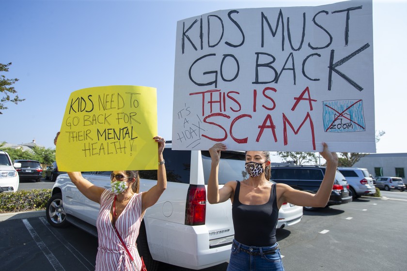 Julia Graham, left, and Karla Rivera hold signs in protest outside of the Newport-Mesa Unified School District offices in Costa Mesa on Oct. 8, 2020. (Scott Smeltzer/ Times Community News)