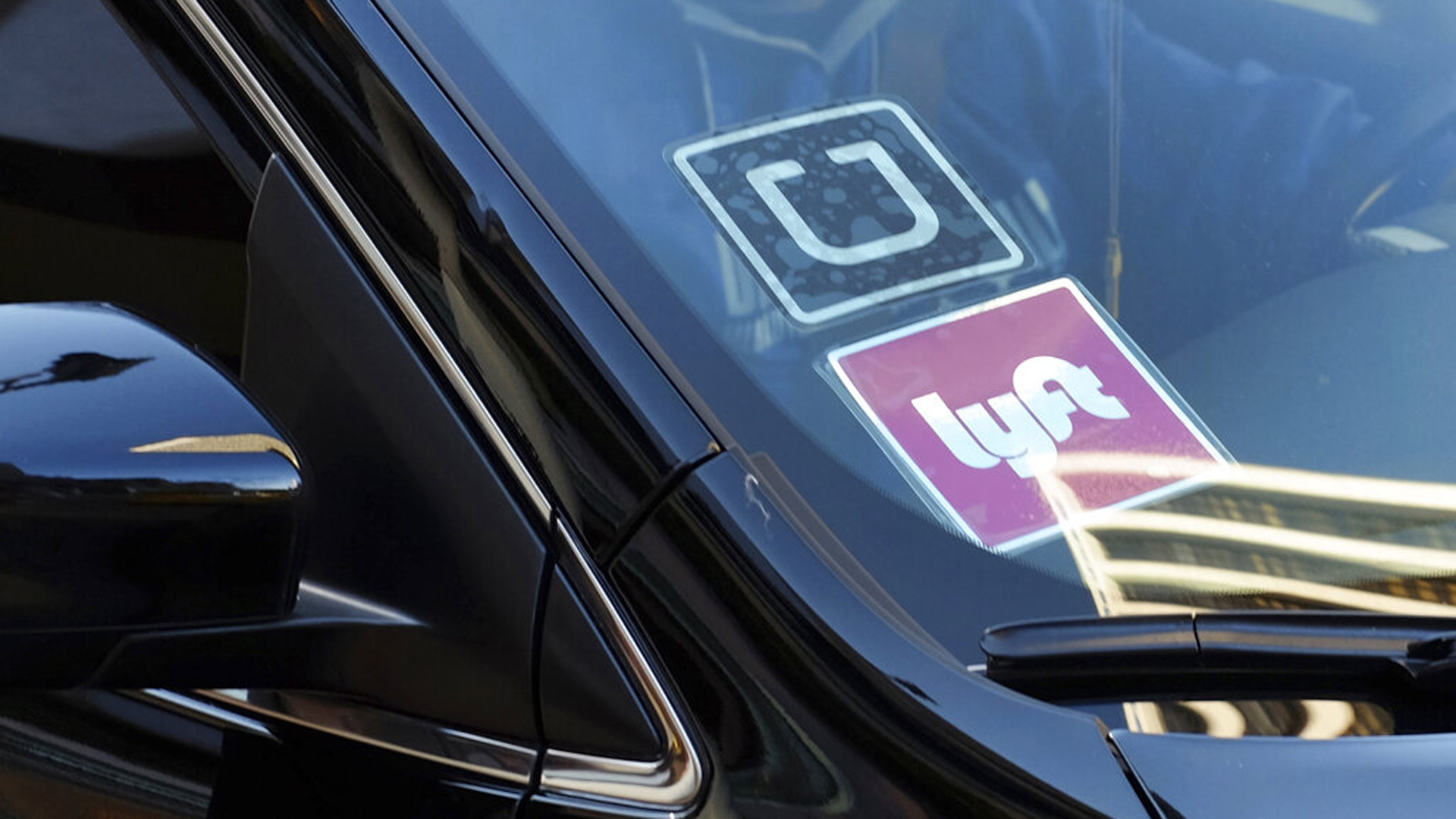 In this Jan. 12, 2016, file photo, a ride share car displays Lyft and Uber stickers on its front windshield in downtown Los Angeles. (Richard Vogel / Associated Press)