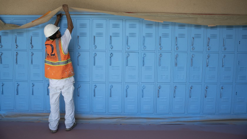 Painting contractor Jose Ortiz tapes a paper mask on along lockers at Oliver Wendell Holmes Middle School in Northridge on Aug. 18, 2020. (Los Angeles Times)