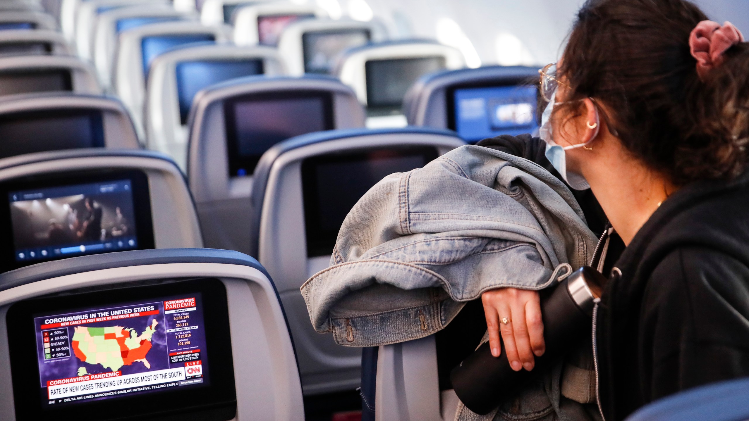 A passenger wears personal protective equipment on a Delta Airlines flight as a map depicting the spread of COVID-19 is displayed on a monitor after landing at Minneapolis−Saint Paul International Airport, Thursday, May 28, 2020, in Minneapolis. (AP Photo/John Minchillo)