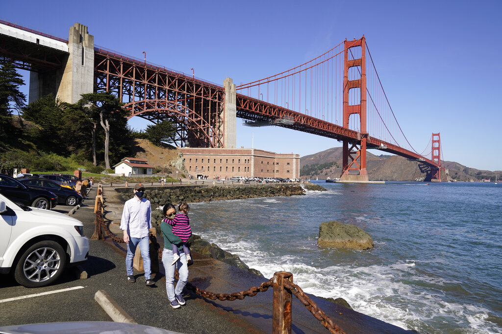 People walk along a seawall with Fort Point and the Golden Gate Bridge in the background in San Francisco on Oct. 11, 2020. (AP Photo/Eric Risberg)