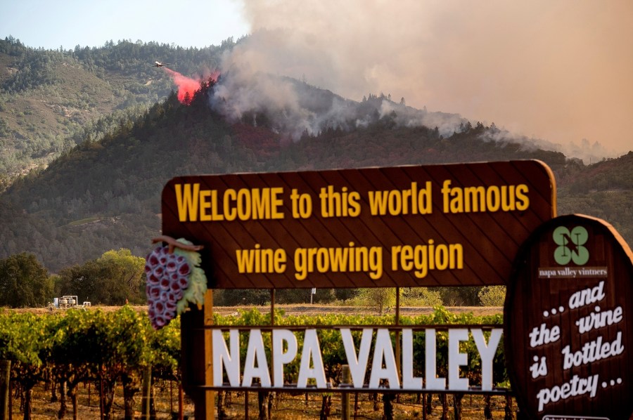 In this Sept. 27, 2020, file photo, an air tanker drops retardant on the Glass Fire burning in Calistoga, Calif. In three of the past four years, major wildfires driven by a changing climate have devastated parts of the world-class region, leaving little doubt that it's vulnerable to smoke, flames and blackouts during the fall. (AP Photo/Noah Berger, File)