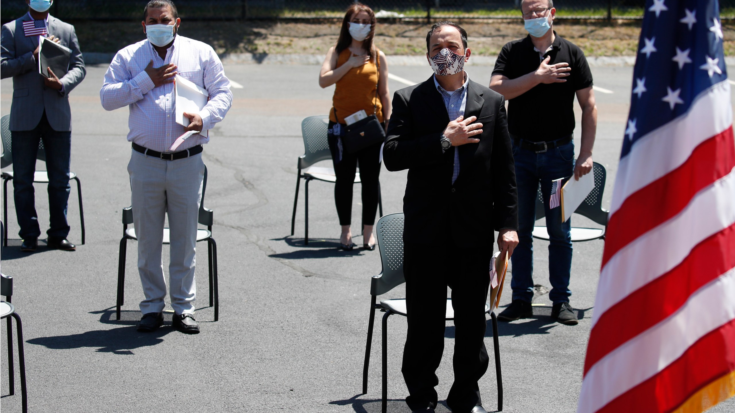 In this June 4, 2020, file photo, new citizens, socially distanced, recite the pledge of allegiance outside the U.S. Citizenship and Immigration Services building in Lawrence, Mass. (AP Photo/Elise Amendola, File)