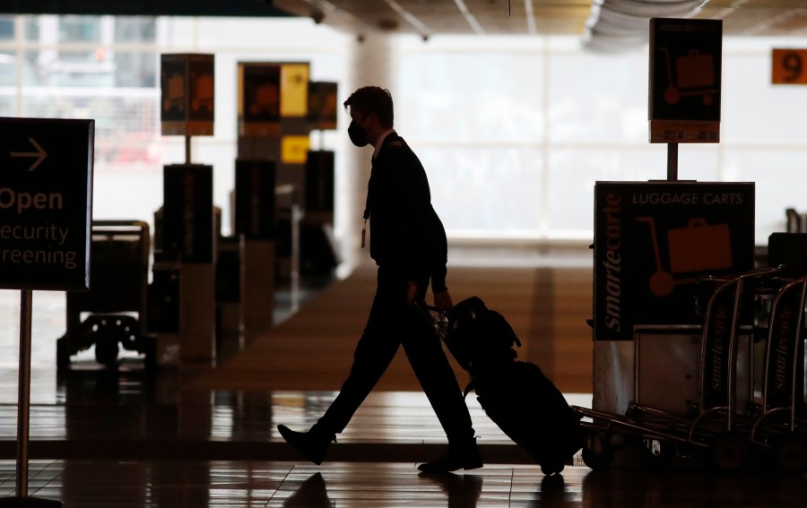 In this Thursday, April 9, 2020, file photo, a lone airline crew member pulls his bags behind him as he walks through the baggage-claim area at Denver International Airport in Denver. (David Zalubowski, File)