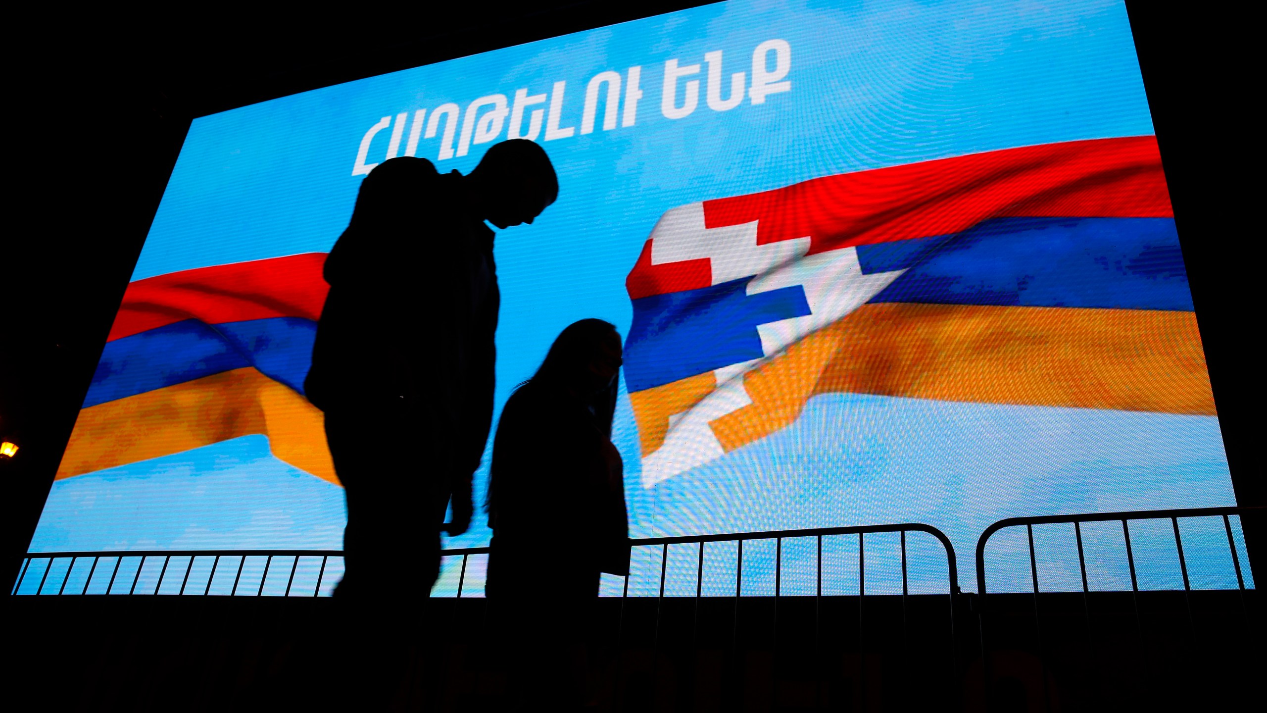 A couple walk past a screen displayed Armenian, left, and Nagorno-Karabakh's flags with sign reading "We will win" in Yerevan, the capital of Armenia on Nov. 9, 2020. (Associated Press)