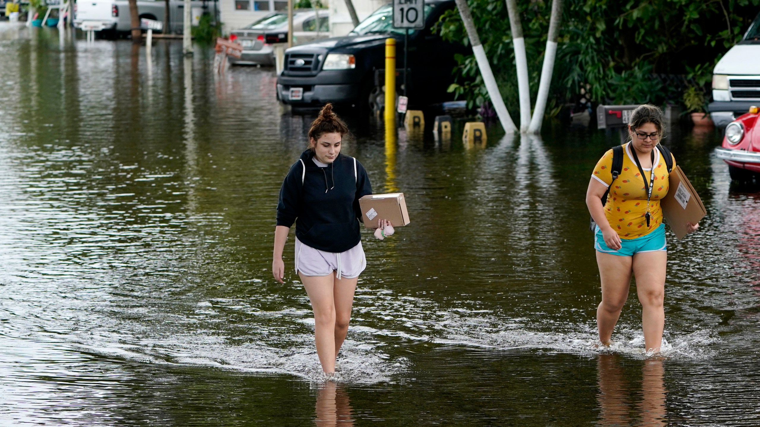 Victoria Rodriguez, left, and Angela Mojica, right, walk on a flooded street in the Driftwood Acres Mobile Home Park, in the aftermath of Tropical Storm Eta, Tuesday, Nov. 10, 2020, in Davie, Fla. (Lynne Sladky/AP Photo)