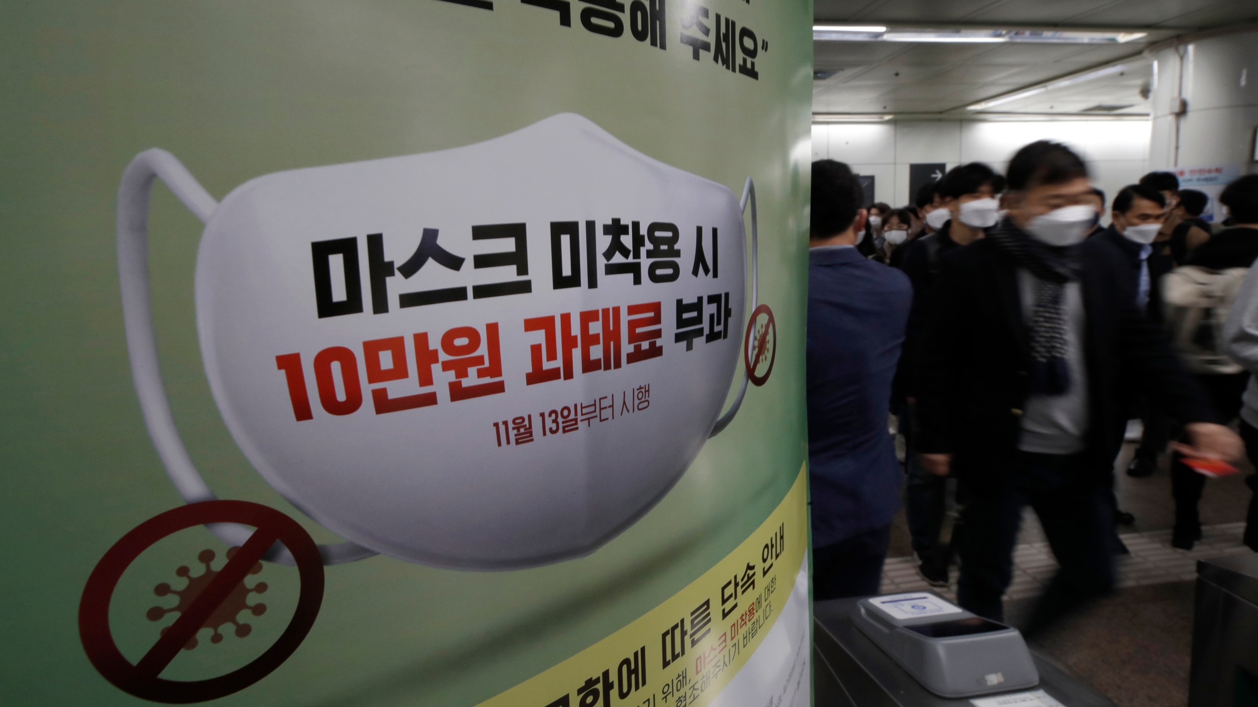 People wearing face masks as a precaution against the coronavirus walk near a banner reading: "People who do not wear masks in public will face a 100,000 won ($90) fine," at a subway station in Seoul, South Korea, on Nov. 13, 2020. (Lee Jin-man / Associated Press)