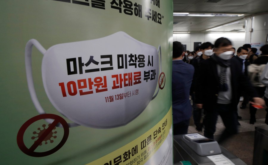 People wearing face masks as a precaution against the coronavirus walk near a banner reading: "People who do not wear masks in public will face a 100,000 won ($90) fine," at a subway station in Seoul, South Korea, on Nov. 13, 2020. (Lee Jin-man / Associated Press)