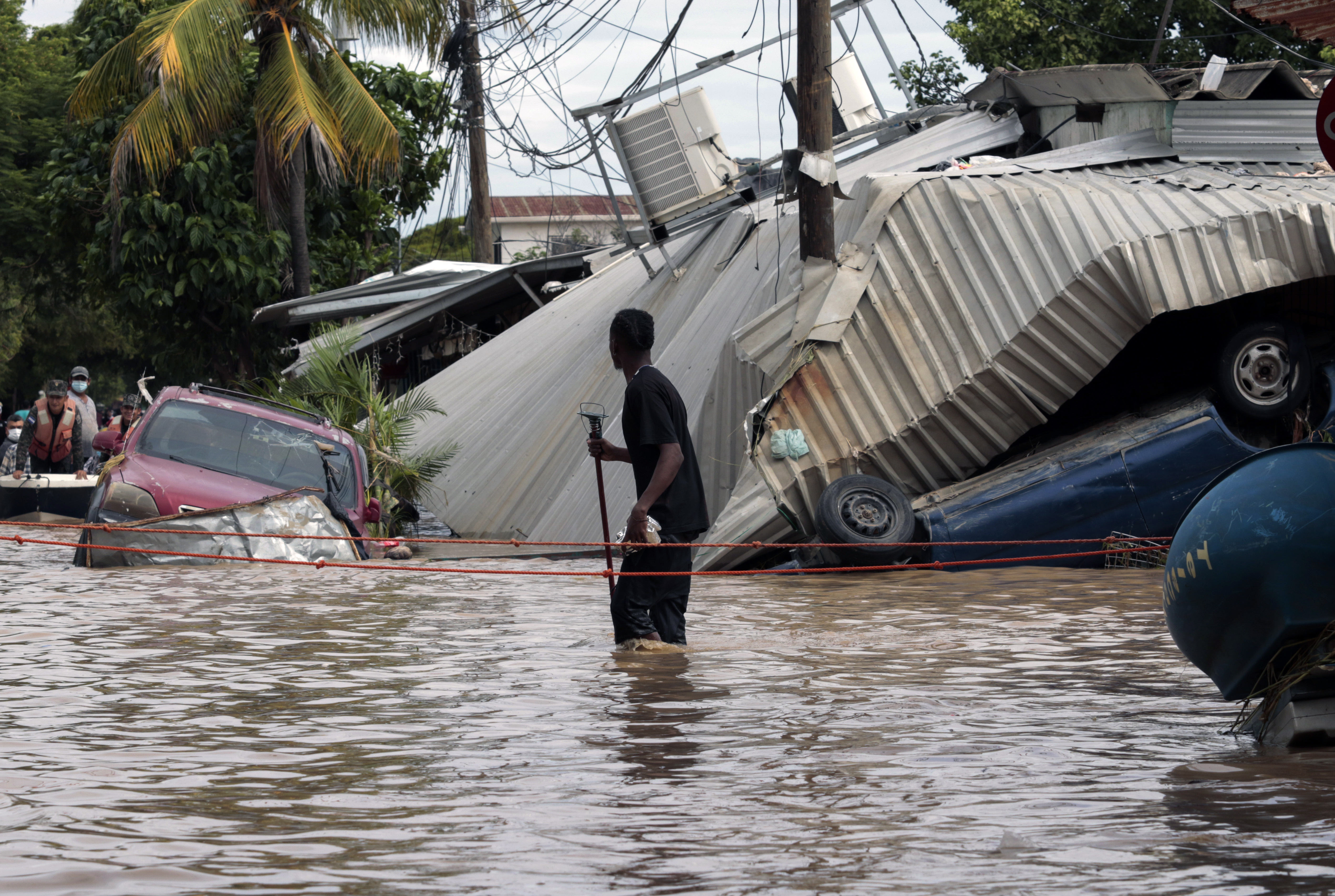 In this Nov. 6, 2020 file photo, a resident walking through a flooded street looks back at storm damage caused by Hurricane Eta in Planeta, Honduras. Flooded out Honduran and Guatemalan families stranded on rooftops in the most marginalized neighborhoods after the passage of hurricanes Eta and Iota portend a new wave of migration, observers across the region say. (AP Photo/Delmer Martinez, File)