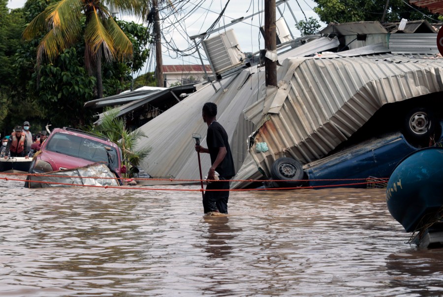 In this Nov. 6, 2020 file photo, a resident walking through a flooded street looks back at storm damage caused by Hurricane Eta in Planeta, Honduras. Flooded out Honduran and Guatemalan families stranded on rooftops in the most marginalized neighborhoods after the passage of hurricanes Eta and Iota portend a new wave of migration, observers across the region say. (AP Photo/Delmer Martinez, File)