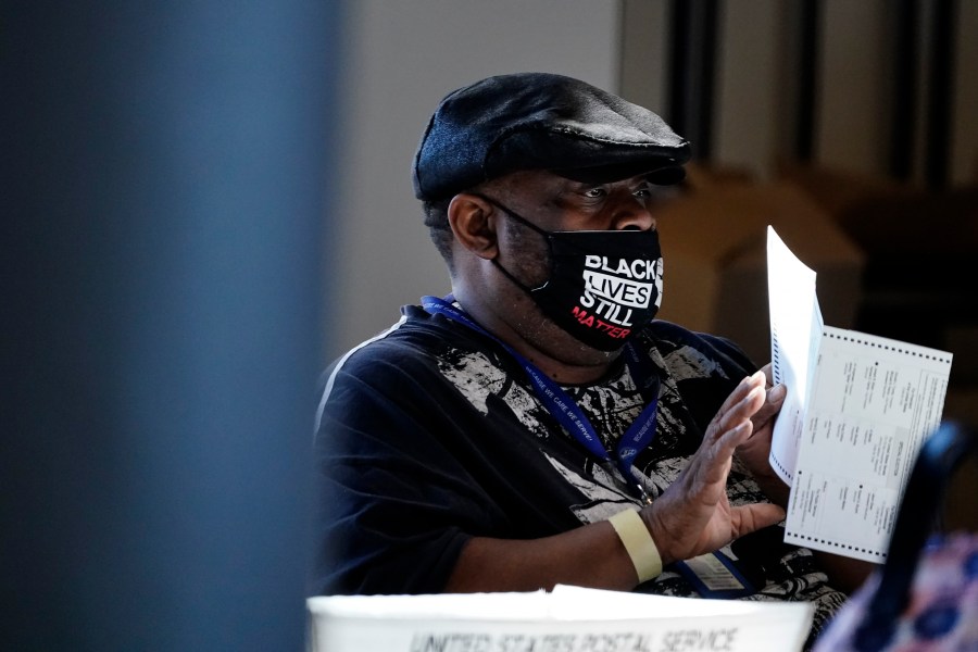 In this Nov. 4, 2020, file photo, an election worker holds a ballot as vote counting in the general election continues at State Farm Arena in Atlanta. President-elect Joe Biden won in Michigan, Wisconsin, Pennsylvania and Georgia because of Black voters, many of them concentrated in big cities. (AP Photo/Brynn Anderson, File)