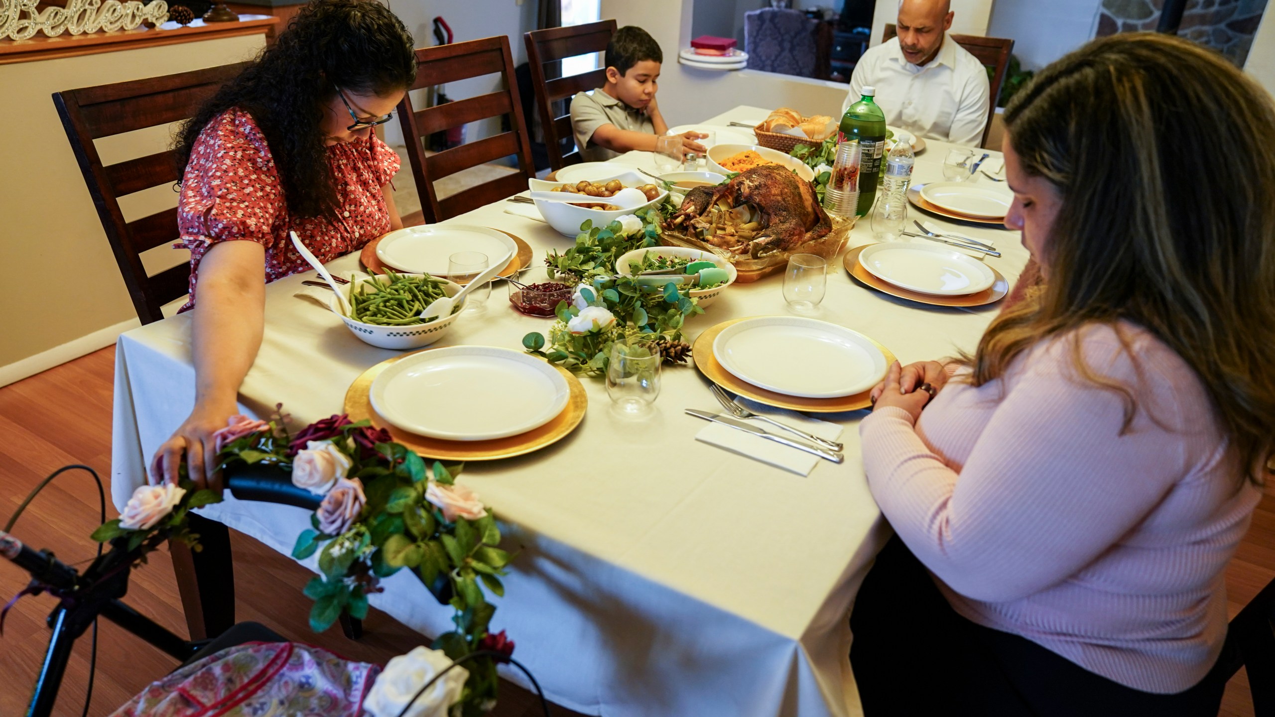 Vivian Zayas holds onto the walker once belonging to her recently deceased mother Ana Martinez while her family prays before Thanksgiving dinner on Nov. 26, 2020, in Deer Park, N.Y. Ana Martinez died at 78 on April 1 while recovering at a nursing home from a knee replacement. (John Minchillo / Associated Press)