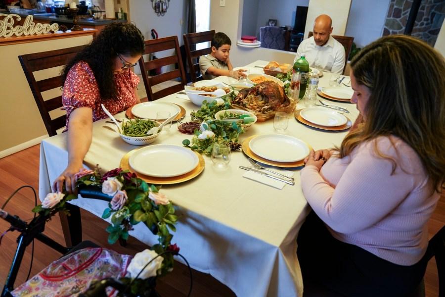 Vivian Zayas holds onto the walker once belonging to her recently deceased mother Ana Martinez while her family prays before Thanksgiving dinner on Nov. 26, 2020, in Deer Park, N.Y. Ana Martinez died at 78 on April 1 while recovering at a nursing home from a knee replacement. (John Minchillo / Associated Press)