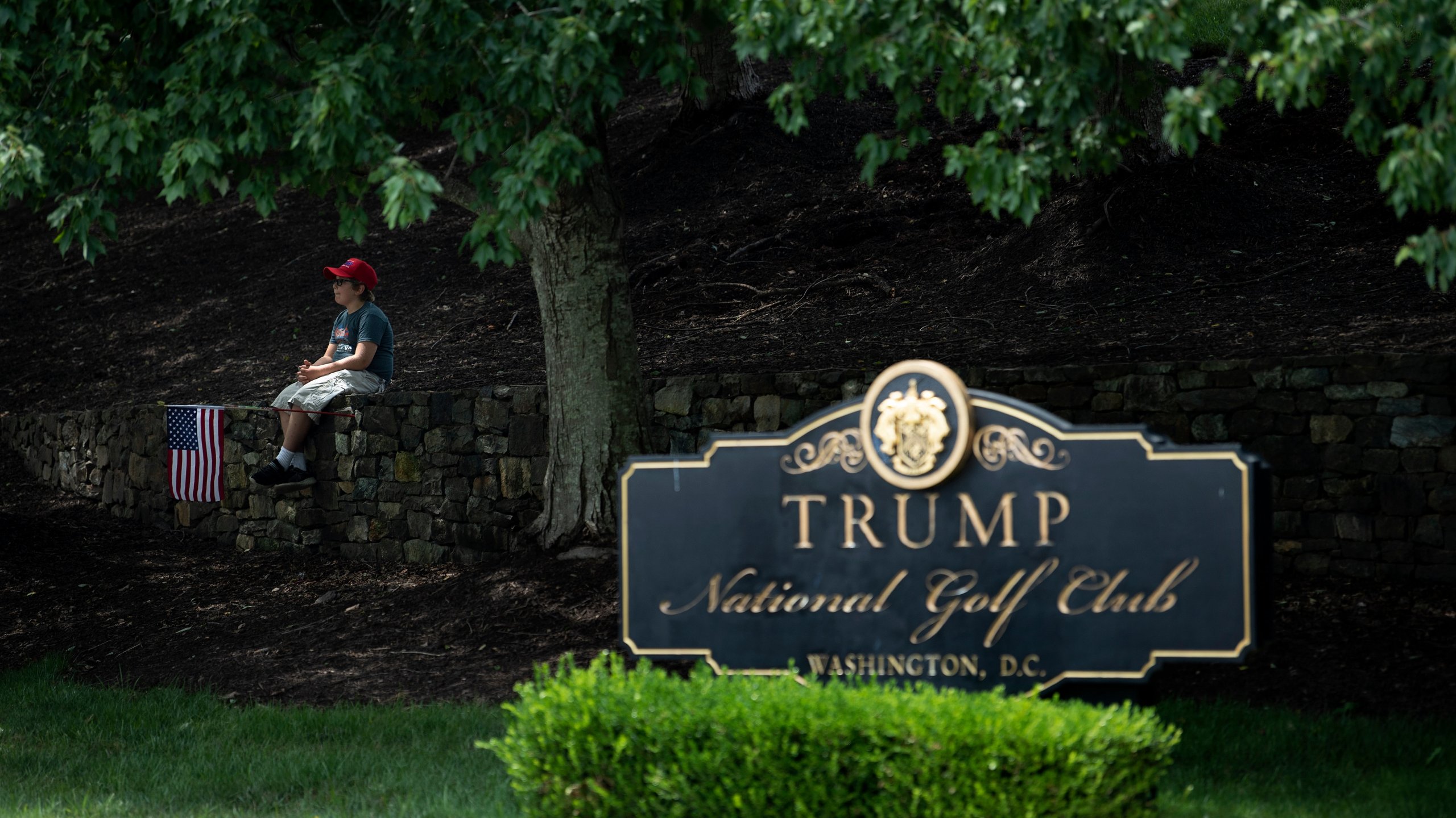 A boy sits on a wall as protesters and supporters of Donald Trump gather outside the Trump National Golf Club as the president golfs at the club on Aug.2, 2020, in Sterling, Virginia. (Brendan Smialowski/AFP via Getty Images)