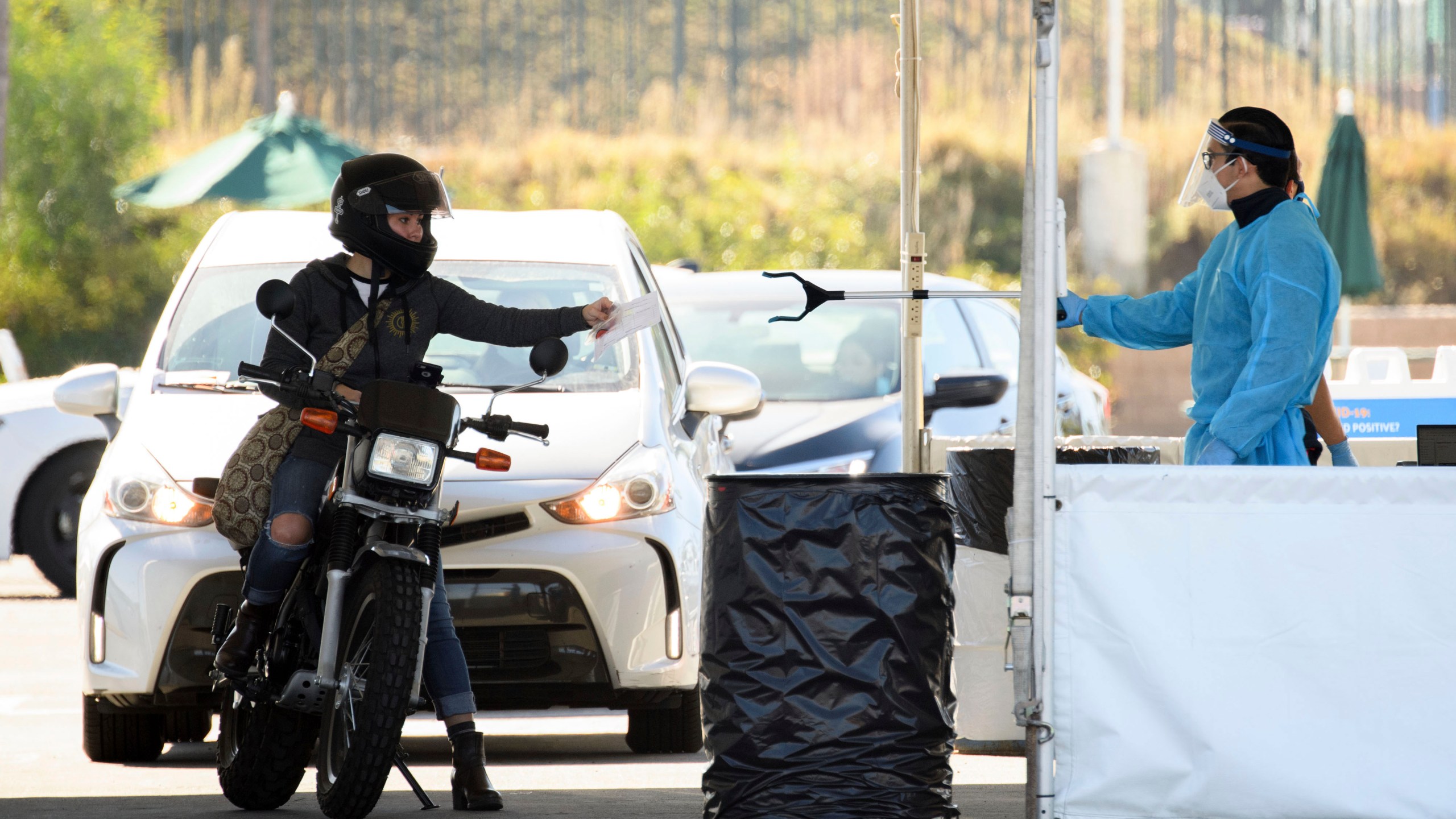 A COVID-19 testing site staff member uses a tool to collect paperwork from a motorcyclist at a drive-up testing site at the Orange County Fairgrounds in Costa Mesa, California, on Nov. 17, 2020. (PATRICK T. FALLON/AFP via Getty Images)