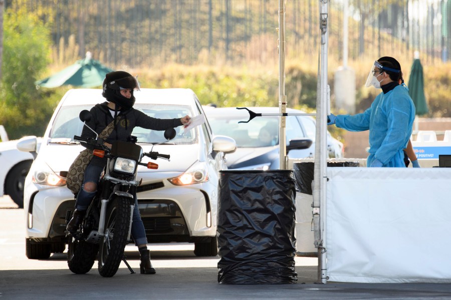 A COVID-19 testing site staff member uses a tool to collect paperwork from a motorcyclist at a drive-up testing site at the Orange County Fairgrounds in Costa Mesa, California, on Nov. 17, 2020. (PATRICK T. FALLON/AFP via Getty Images)