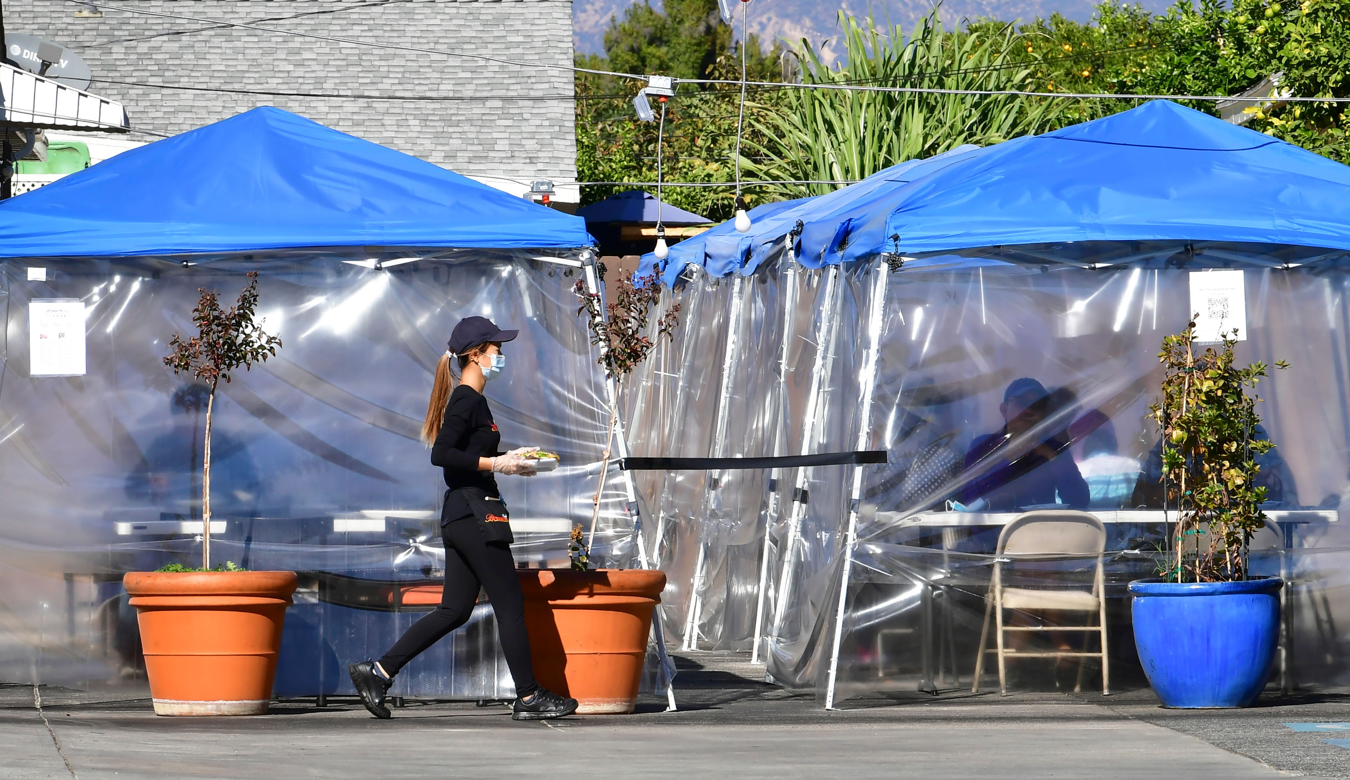 A waitress delivers orders to diners seated outdoors under tents in a restaurant's parking lot on Nov. 17, 2020 in Alhambra. (FREDERIC J. BROWN/AFP via Getty Images)