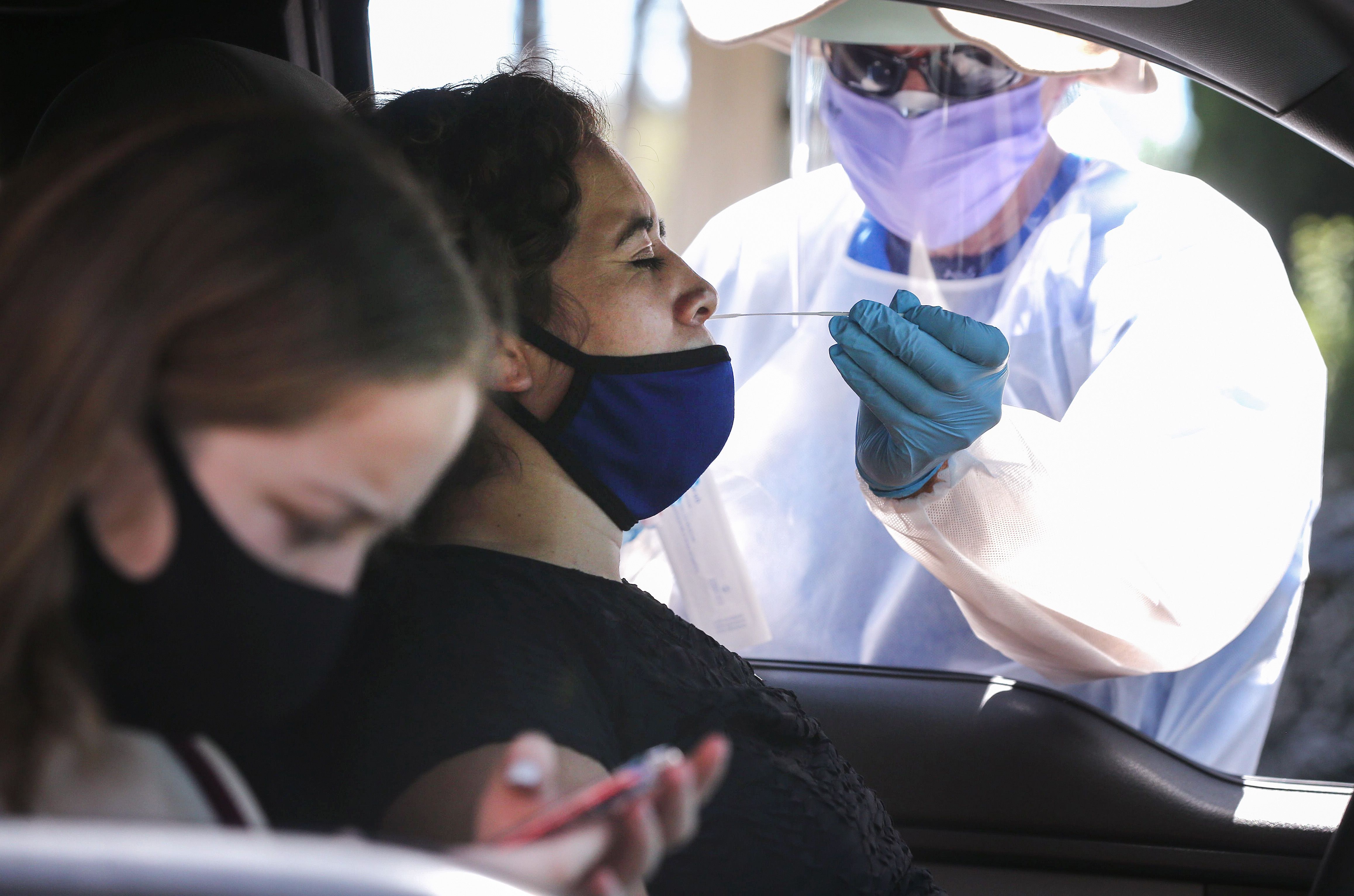 A healthcare worker assists a motorist with a nasal swab test at a drive-in coronavirus testing center on Aug.11, 2020 in Los Angeles. (Mario Tama/Getty Images)