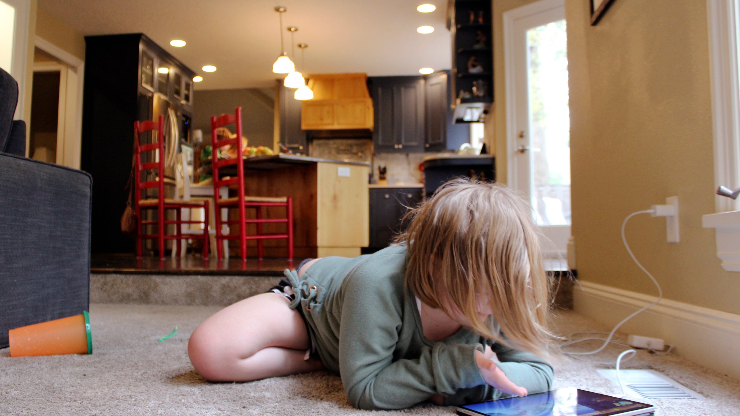 Lizzie Dale sprawls on the floor to play games on an iPad as her siblings work on school work in the kitchen behind her in their home in Lake Oswego, Ore., Oct. 30, 2020. (Sara Cline/AP Photo)