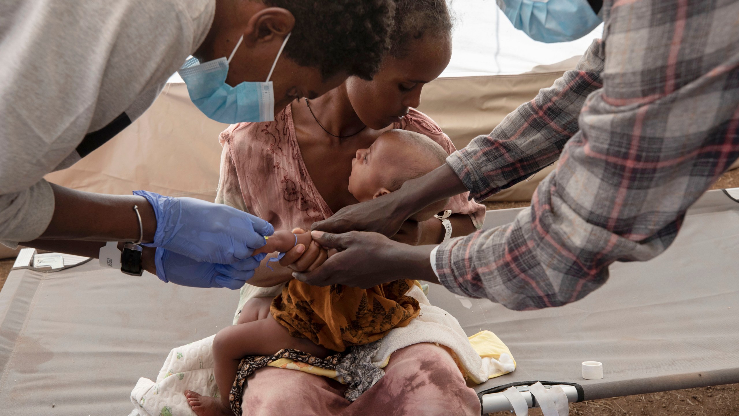 A Tigray woman who fled the conflict in Ethiopia's Tigray region, holds her malnourished and severely dehydrated baby as nurses give him IV fluids, at the Medecins Sans Frontieres (MSF) clinic, at Umm Rakouba refugee camp in Qadarif, eastern Sudan, Saturday, Dec. 5, 2020. (Nariman El-Mofty/AP Photo)