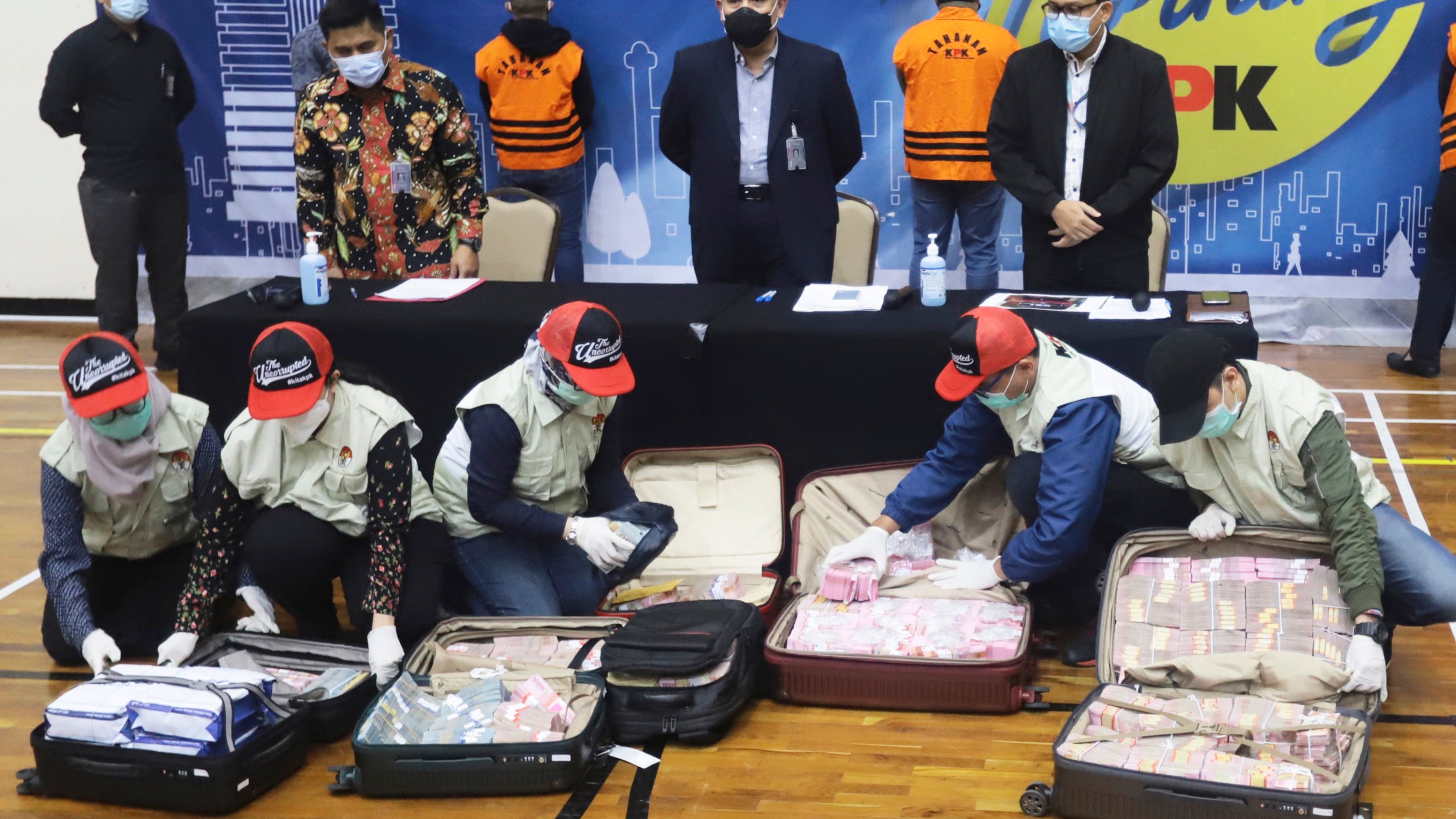 Officers arrange suitcases full of rupiah and U.S. dollar bills confiscated from suspects as Chairman of Indonesia's Corruption Eradication Commission Firli Bahuri, top center, looks on during a news conference on a corruption case involving government's COVID-19 pandemic aid distribution, in Jakarta, Indonesia, Sunday, Dec. 6, 2020. (Birendra/AP Photo)