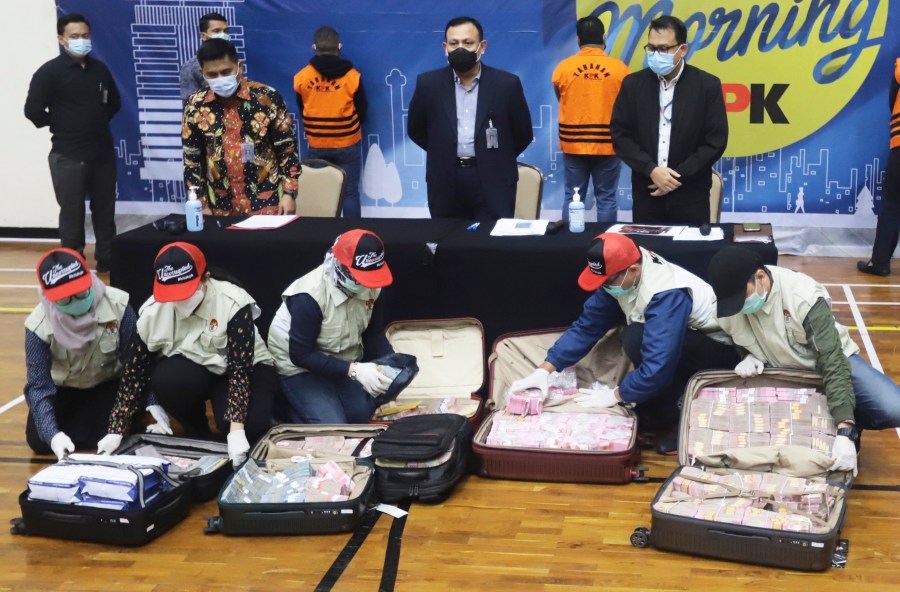 Officers arrange suitcases full of rupiah and U.S. dollar bills confiscated from suspects as Chairman of Indonesia's Corruption Eradication Commission Firli Bahuri, top center, looks on during a news conference on a corruption case involving government's COVID-19 pandemic aid distribution, in Jakarta, Indonesia, Sunday, Dec. 6, 2020. (Birendra/AP Photo)