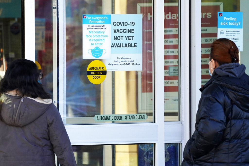 In this Dec. 4, 2020, file photo, customers wear a mask as they check out information signs that a COVID-19 vaccine is not yet available at Walgreens in Northbrook, Ill. (AP Photo/Nam Y. Huh, File)