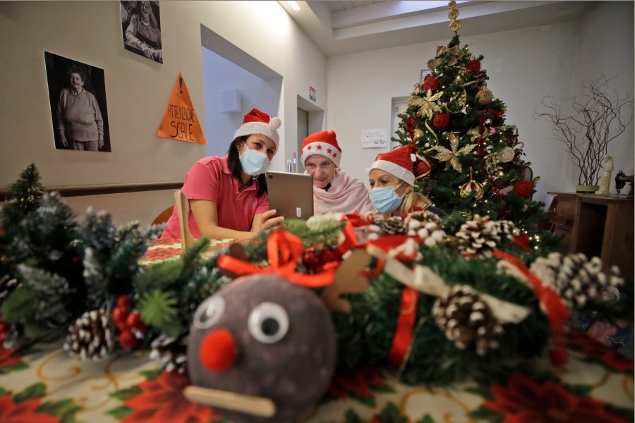 In this Dec. 19, 2020, file photo, Augusta Grigis, is flanked by nurse Michela Valle, left, and director Maria Giulia Madaschi, as she talks via a tablet with a donor who bought and sent her a Christmas present through an organization dubbed "Santa's Grandchildren", at a nursing home in Alzano Lombardo, in Northern Italy. (Luca Bruno/AP Photo)