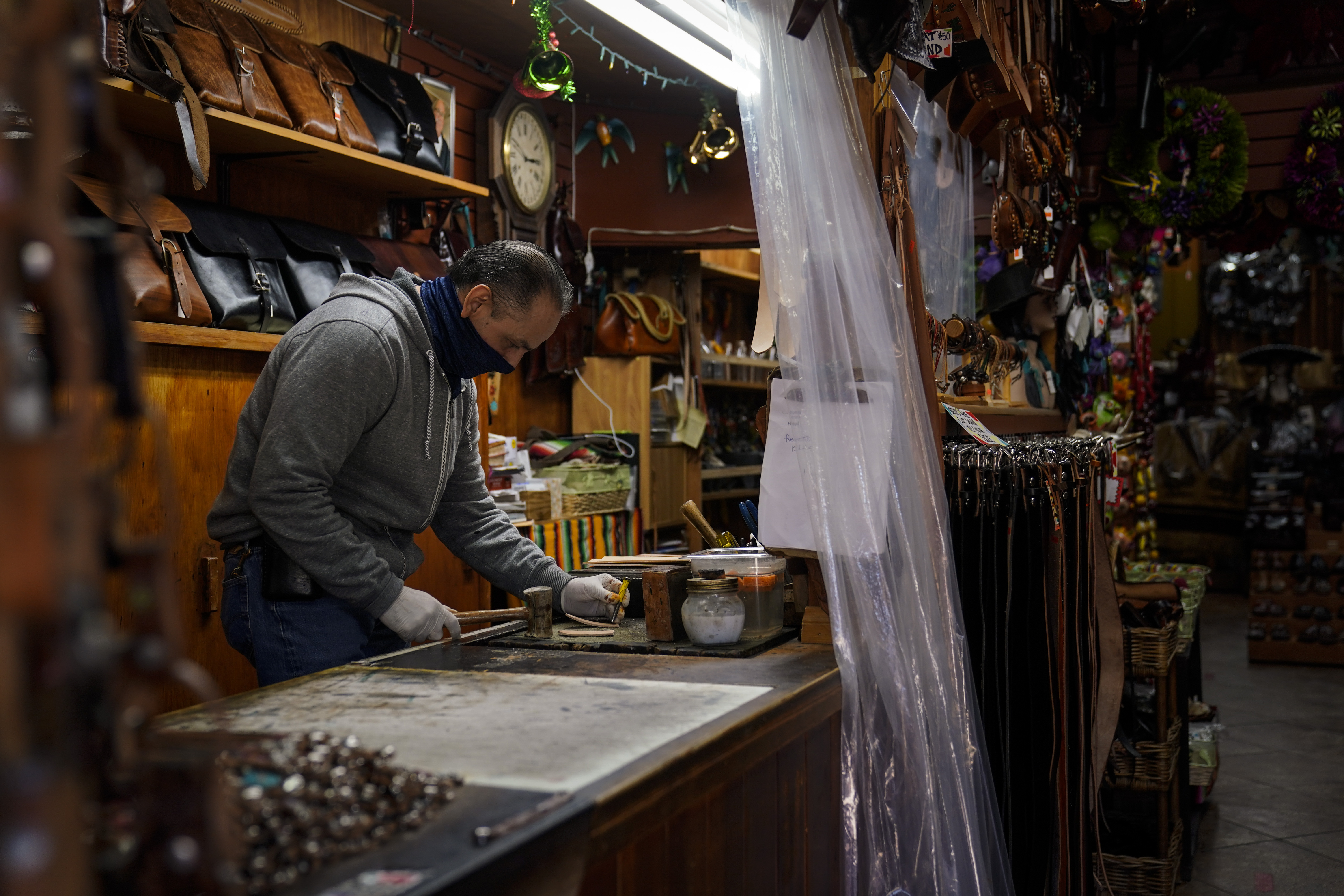 Leather artisan Armando Murillo works in his shop on Olvera Street in downtown Los Angeles, Wednesday, Dec. 16, 2020. Olvera Street, known as the birthplace of Los Angeles, has been particularly hard hit by the coronavirus pandemic, with shops and restaurants closed and others barely hanging on. Only a handful of businesses remain open on weekdays as tourism has cratered and downtown offices are closed and festive events held throughout the year have been canceled. (Jae C. Hong / Associated Press)