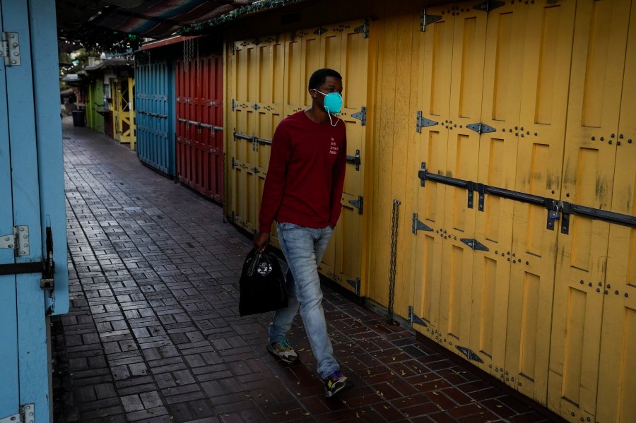 A man wearing a face mask walks past shuttered market stalls on empty Olvera Street in downtown Los Angeles, Tuesday, Dec. 15, 2020. The tree-covered brick alley typically teeming with tourists is empty. Many of the shops that sell everything from traditional Mexican folk dresses to paintings of artist Frida Kahlo to sombreros are padlocked and the ones open have few, if any, customers. (Jae C. Hong / Associated Press)