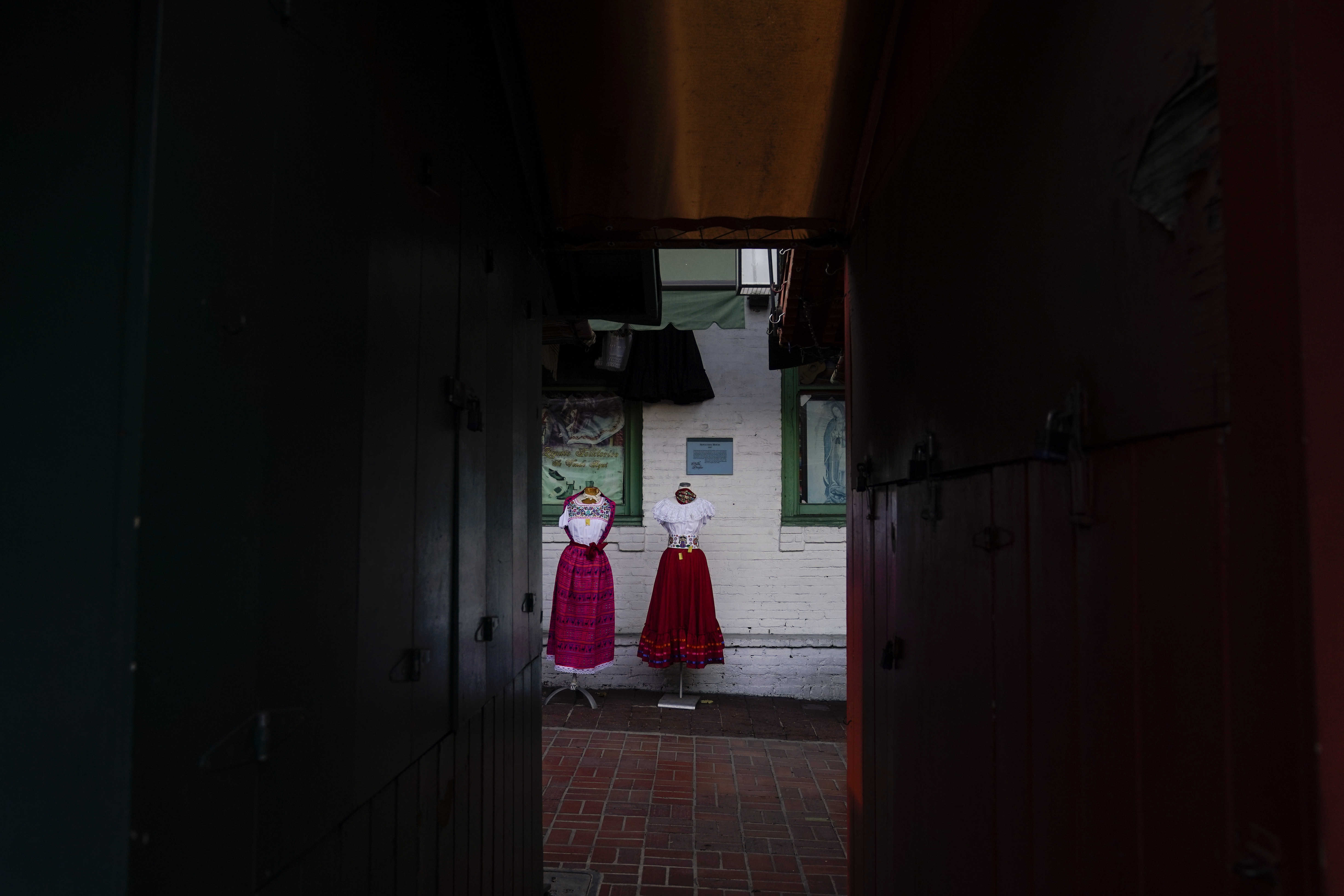 Traditional Mexican folk dresses are seen between shuttered market stalls on Olvera Street in downtown Los Angeles, Tuesday, Dec. 15, 2020. The tree-covered brick alley typically teeming with tourists is empty. Many of the shops that sell everything from traditional Mexican folk dresses to paintings of artist Frida Kahlo to sombreros are padlocked and the ones open have few, if any, customers. (Jae C. Hong / Associated Press)