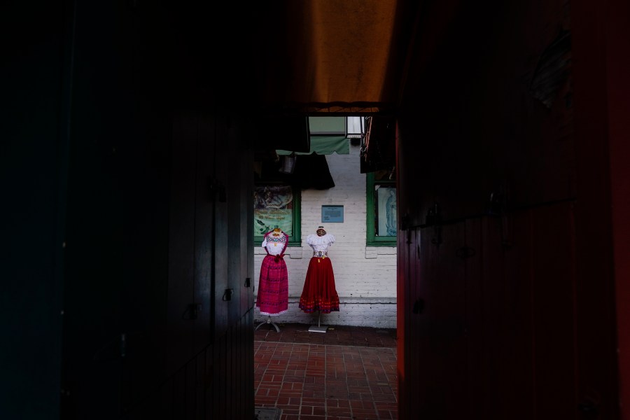 Traditional Mexican folk dresses are seen between shuttered market stalls on Olvera Street in downtown Los Angeles, Tuesday, Dec. 15, 2020. The tree-covered brick alley typically teeming with tourists is empty. Many of the shops that sell everything from traditional Mexican folk dresses to paintings of artist Frida Kahlo to sombreros are padlocked and the ones open have few, if any, customers. (Jae C. Hong / Associated Press)