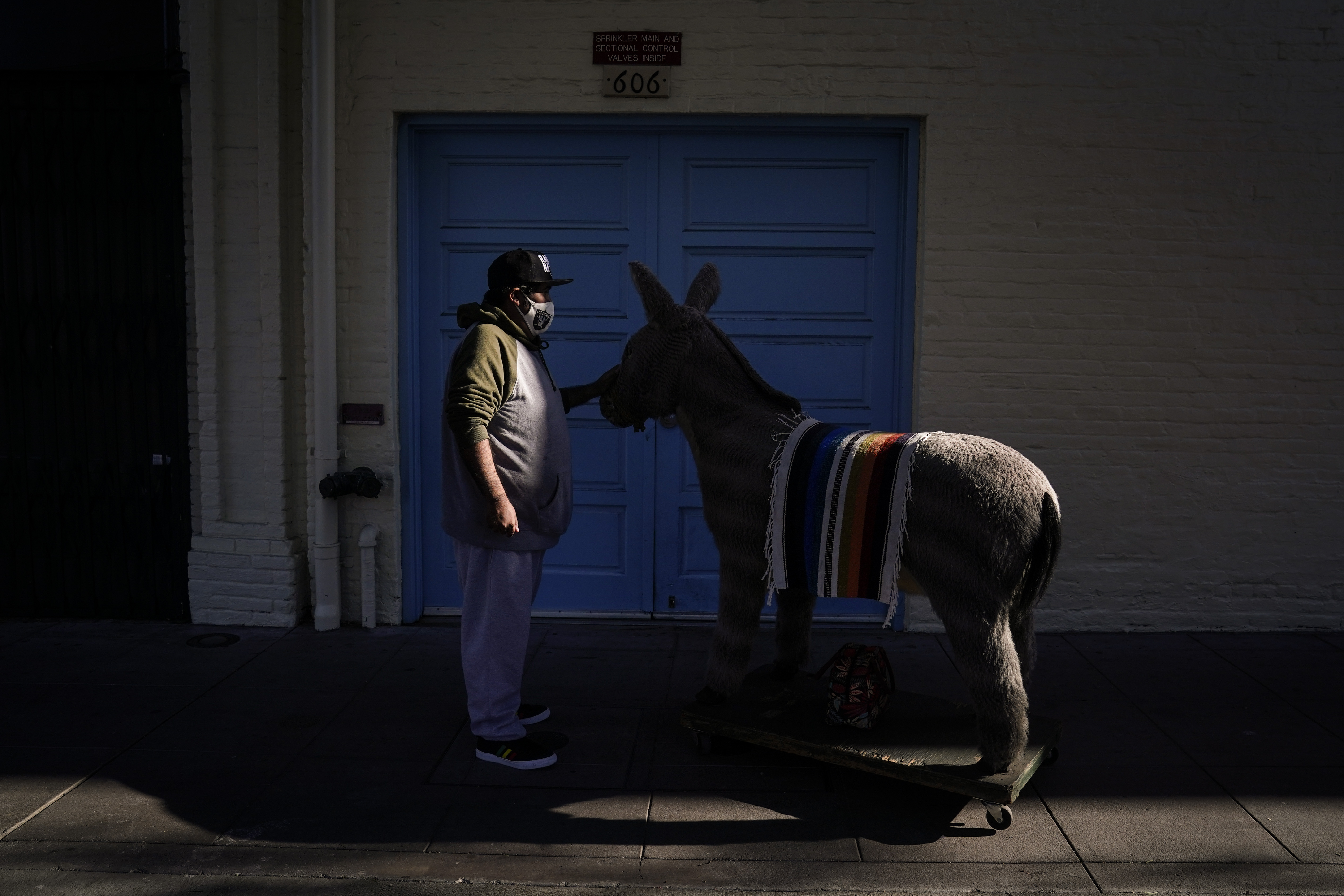 Jesus Hernandez, a merchant who owns a gift shop on Olvera Street that only opens on weekends due to the pandemic, waits for a key to store his uncle's life-size stuffed donkey, a photo prop named George, in downtown Los Angeles, Wednesday, Dec. 16, 2020. Olvera Street, known as the birthplace of Los Angeles, has been particularly hard hit by the coronavirus pandemic, with shops and restaurants closed and others barely hanging on. (Jae C. Hong / Associated Press)