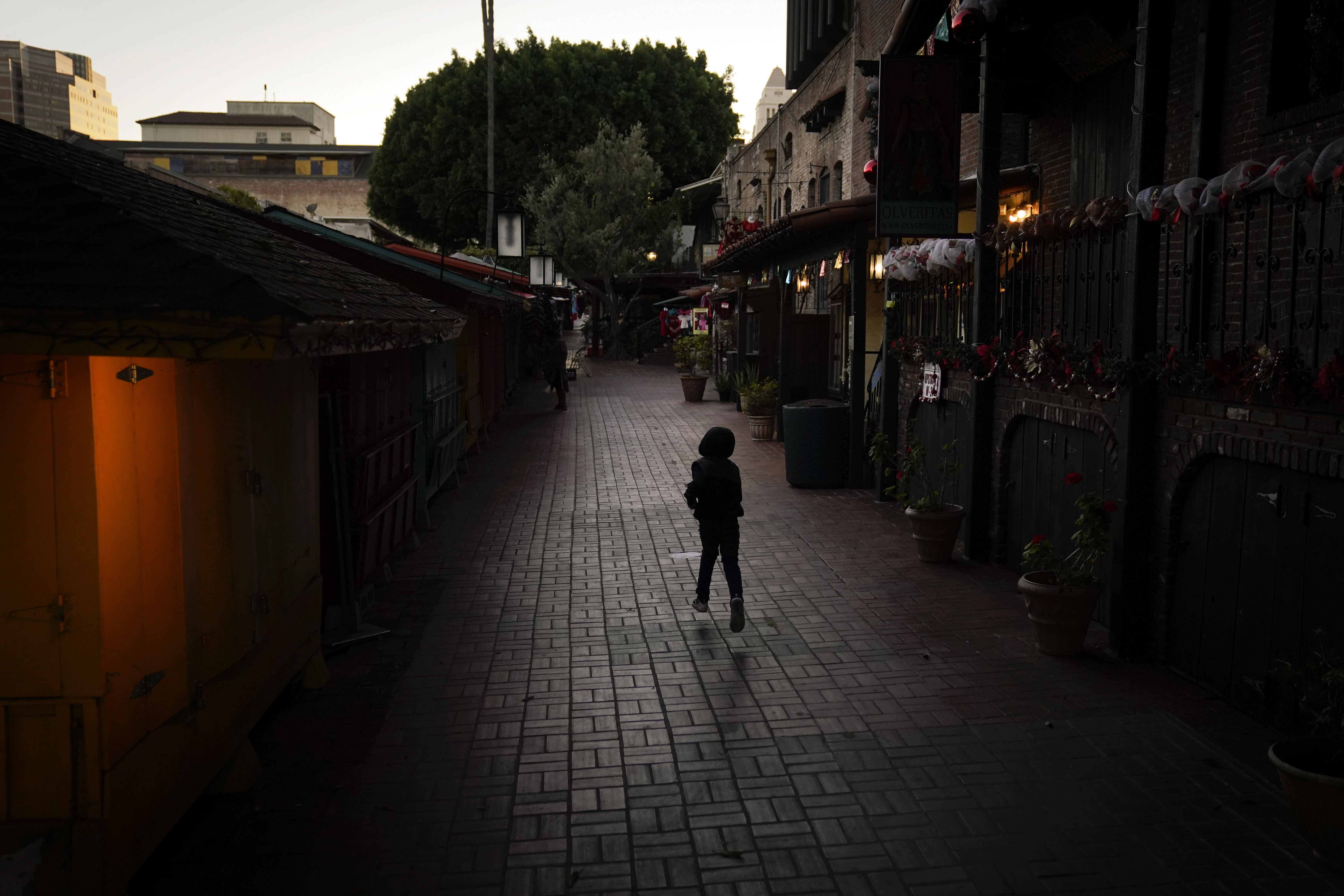 A boy chases a bird on an empty Olvera Street in downtown Los Angeles, Tuesday, Dec. 15, 2020. The tree-covered brick alley typically teeming with tourists is empty. Many of the shops that sell everything from traditional Mexican folk dresses to paintings of artist Frida Kahlo to sombreros are padlocked and the ones open have few, if any, customers. The strains of mariachi trios have fallen silent and the fragrance of taquitos frying has become less pungent. (Jae C. Hong / Associated Press)