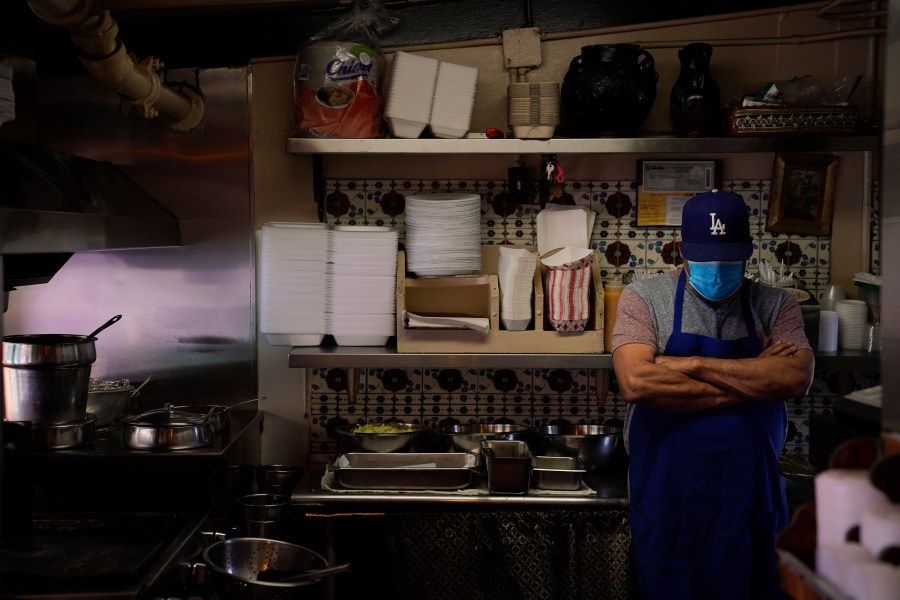 Valo Martinez, a 63-year-old cook working at El Rancho Grande, waits for customers on Olvera Street in downtown Los Angeles, Wednesday, Dec. 16, 2020. The tree-covered brick alley typically teeming with tourists is empty. Many of the shops that sell everything from traditional Mexican folk dresses to paintings of artist Frida Kahlo to sombreros are padlocked and the ones open have few, if any, customers. (Jae C. Hong / Associated Press)