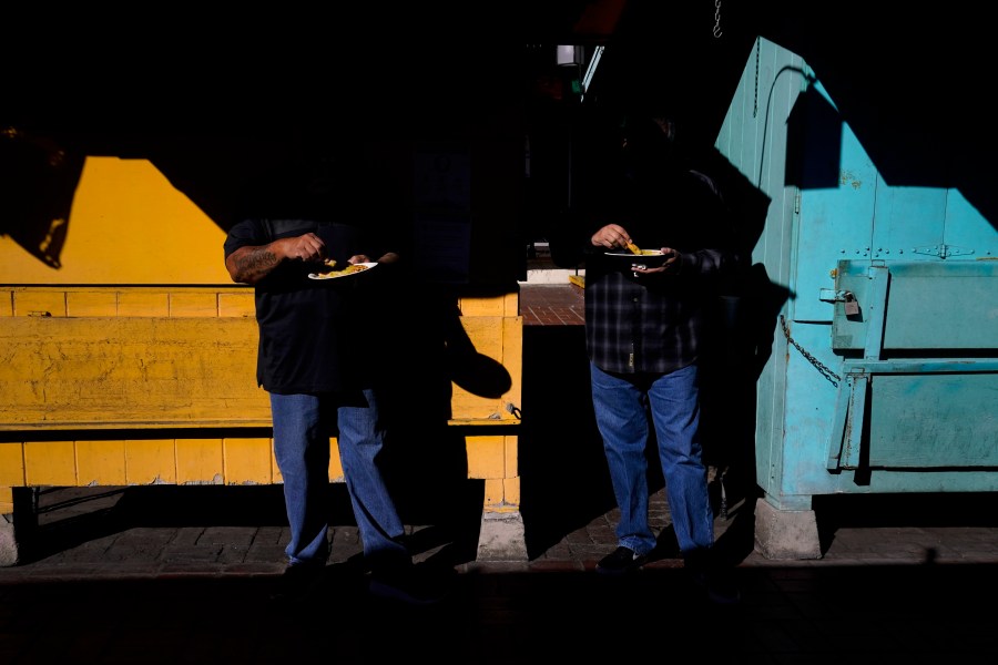 Two customers eat their lunch in front of shuttered market stalls on Olvera Street in downtown Los Angeles, Wednesday, Dec. 16, 2020. Olvera Street, known as the birthplace of Los Angeles, has been particularly hard hit by the coronavirus pandemic, with shops and restaurants closed and others barely hanging on. Only a handful of businesses remain open on weekdays as tourism has cratered and downtown offices are closed and festive events held throughout the year have been canceled. (Jae C. Hong / Associated Press)