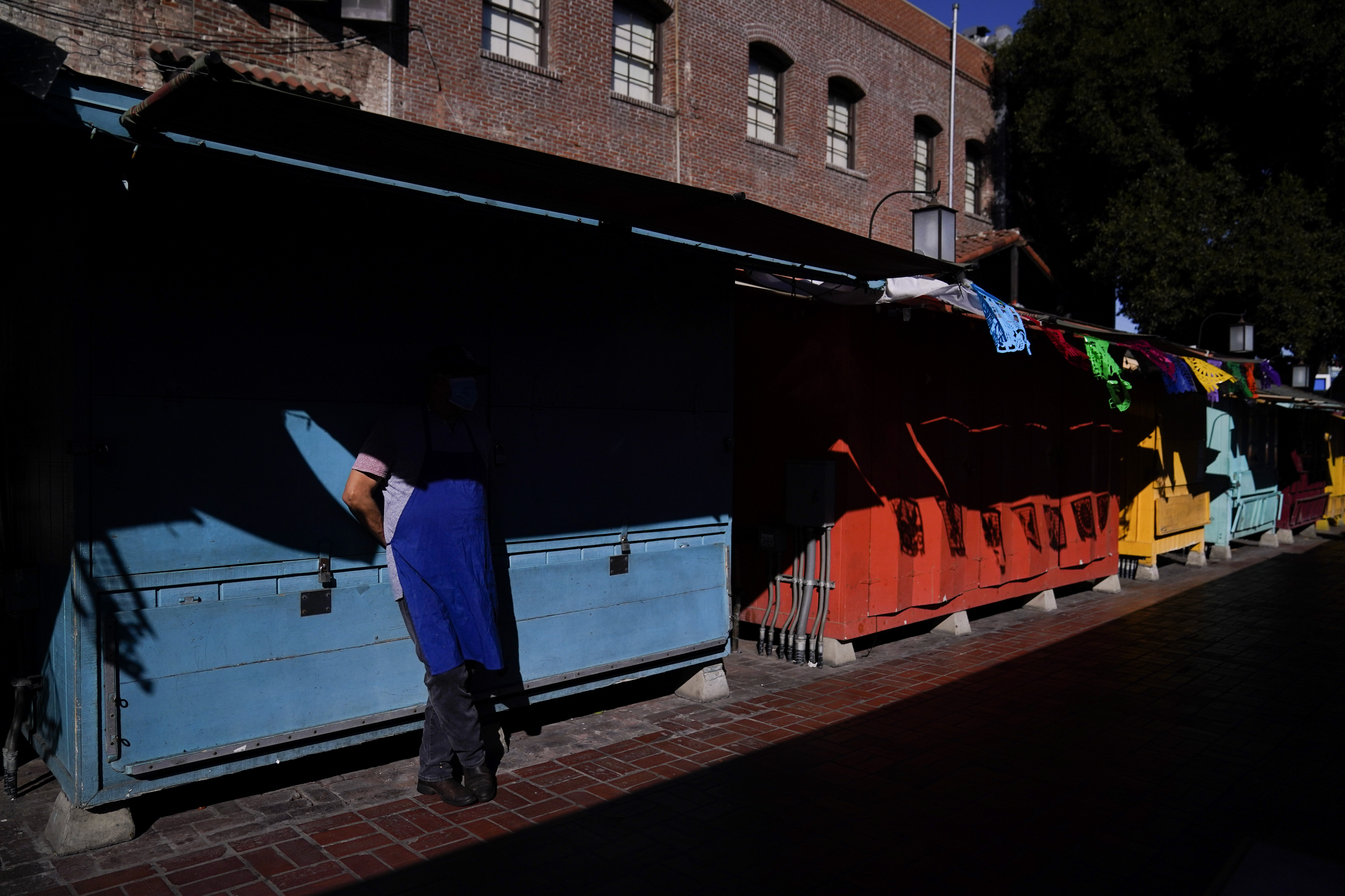 Valo Martinez, a 63-year-old cook working at El Rancho Grande, waits for customers on Olvera Street lined with shuttered market stalls in downtown Los Angeles, Wednesday, Dec. 16, 2020. Olvera Street, known as the birthplace of Los Angeles, has been particularly hard hit by the coronavirus pandemic, with shops and restaurants closed and others barely hanging on. Only a handful of businesses remain open on weekdays as tourism has cratered and downtown offices are closed and festive events held throughout the year have been canceled. (Jae C. Hong / Associated Press)